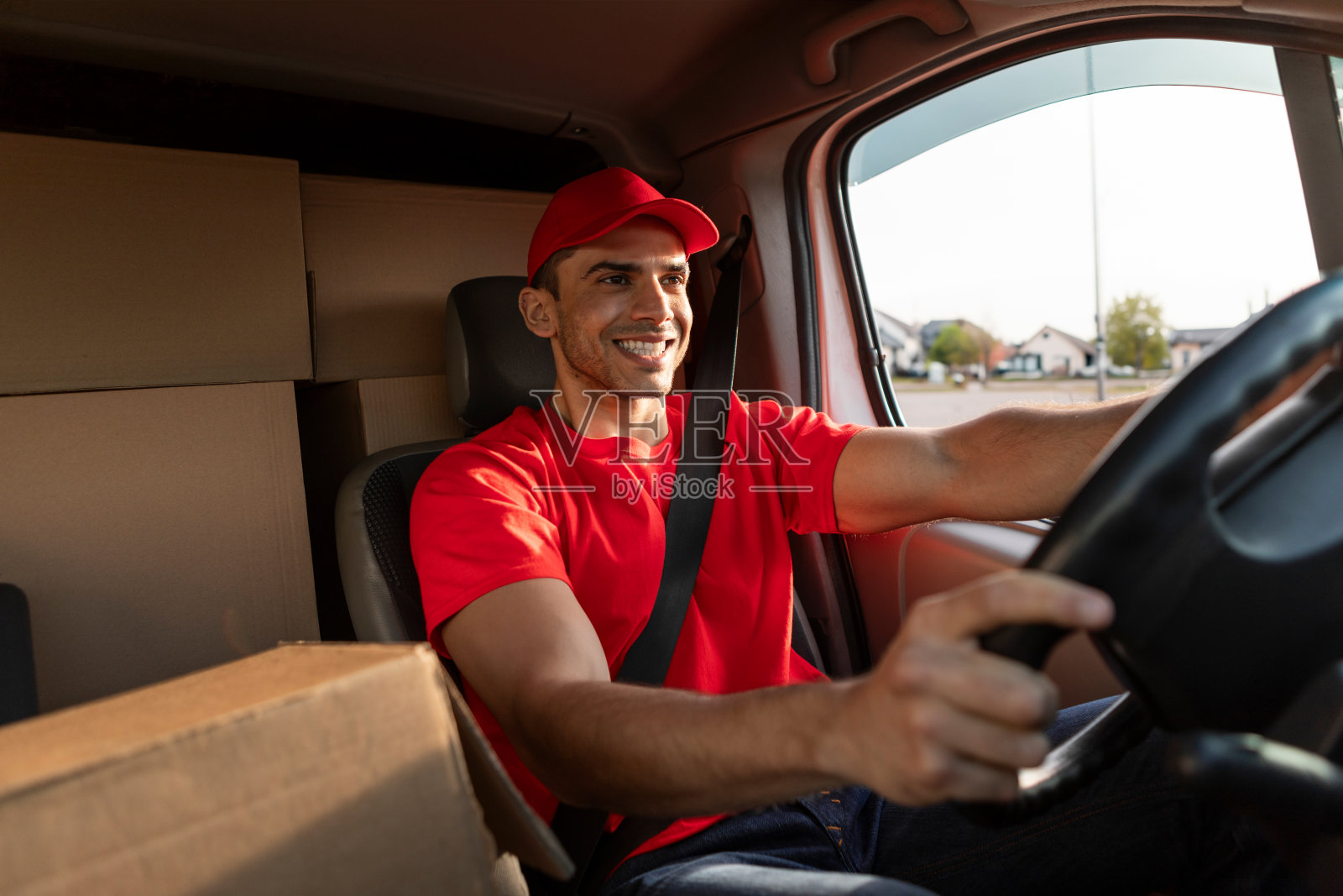 快递员开着快递车，车里装满了包裹，小伙子拿着方向盘，面带微笑照片摄影图片