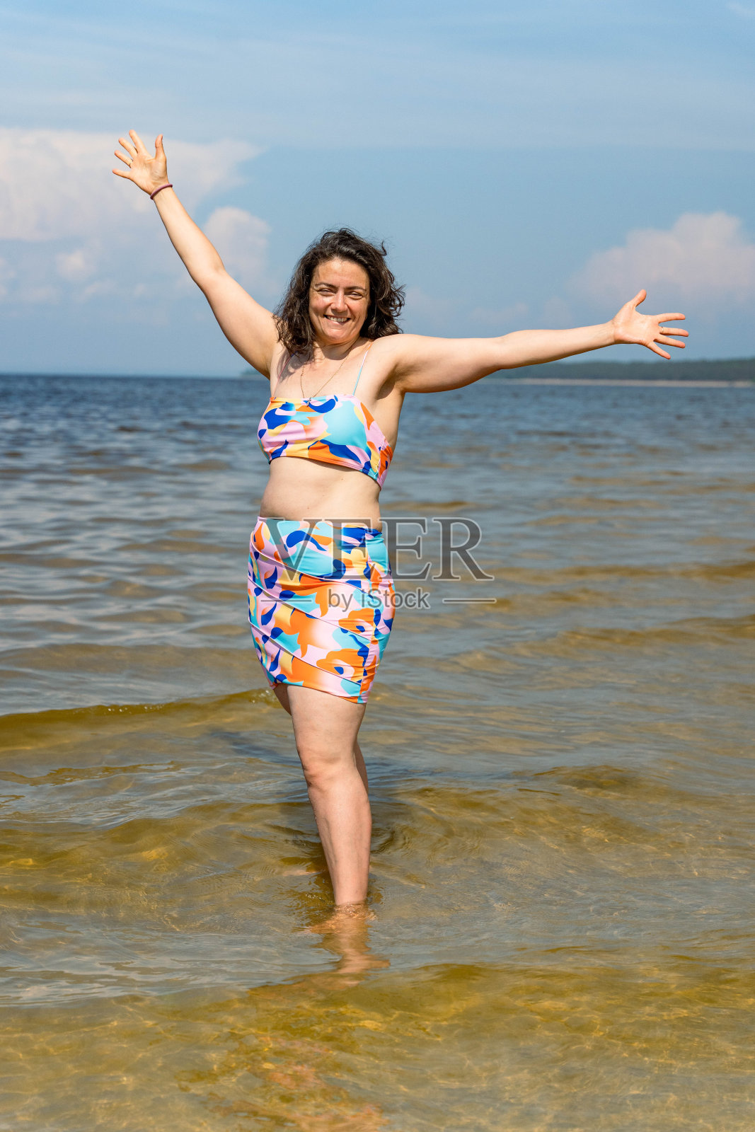 穿着鲜艳泳装的女人在海湾浅滩上微笑。身体呈阳性，丰满，脂肪团照片摄影图片
