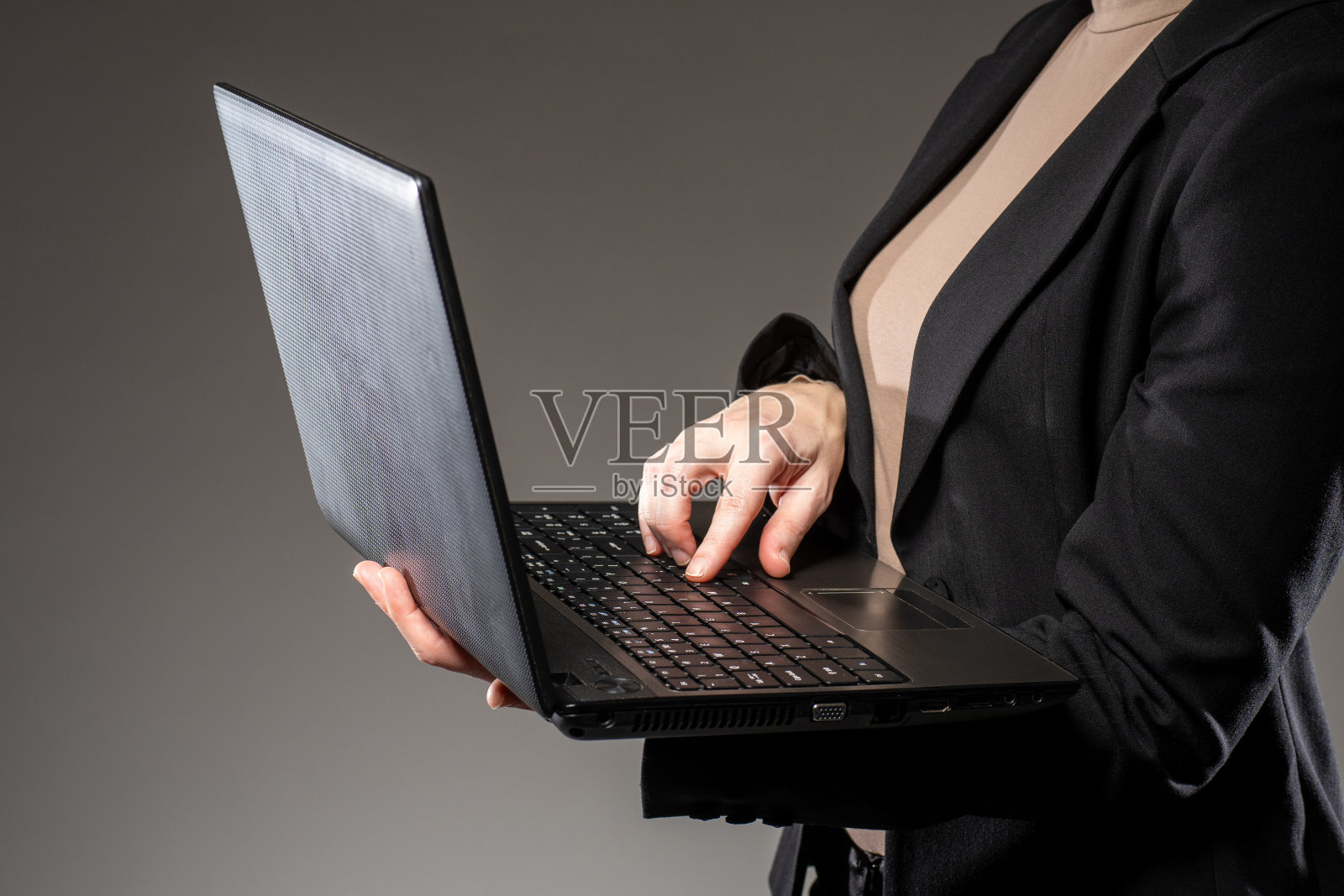 一个站着的人手里拿着笔记本电脑。女人站着用笔记本电脑。拿着笔记本电脑的女商人。概念-商业软件。商务软件。商业计算机应用照片摄影图片