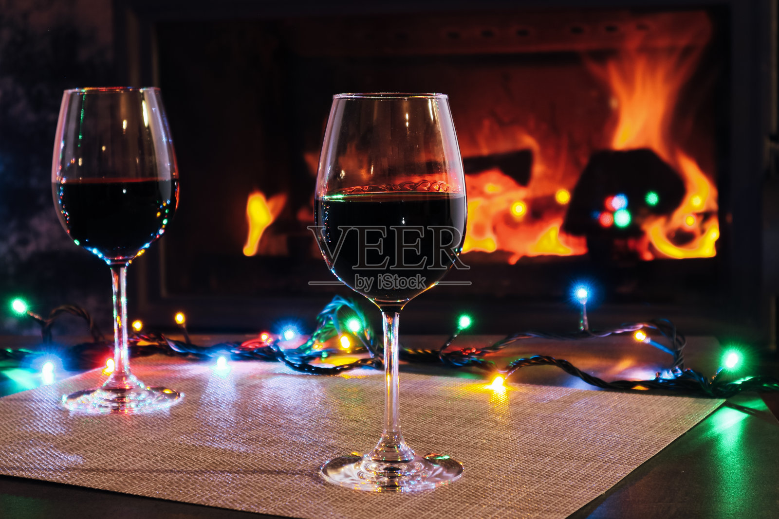 两个红色的酒杯和灯光装饰在燃烧的壁炉背景。壁炉边的酒。照片摄影图片