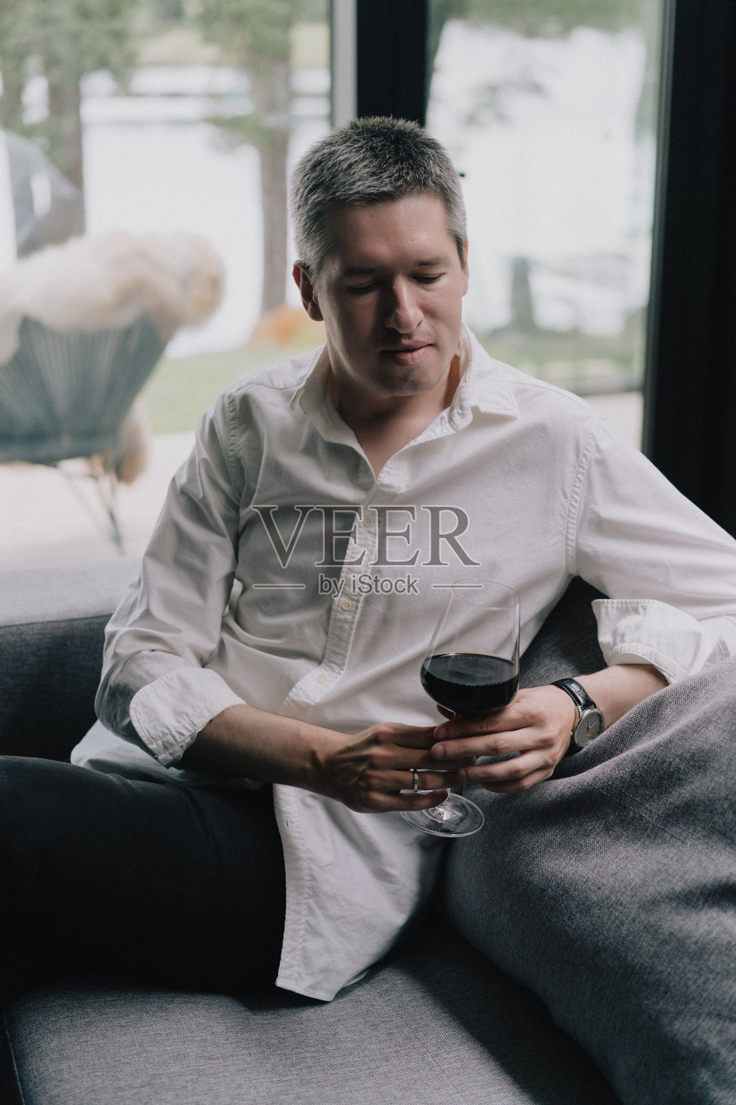 一个男人坐在沙发上，手里拿着一杯红酒。照片摄影图片