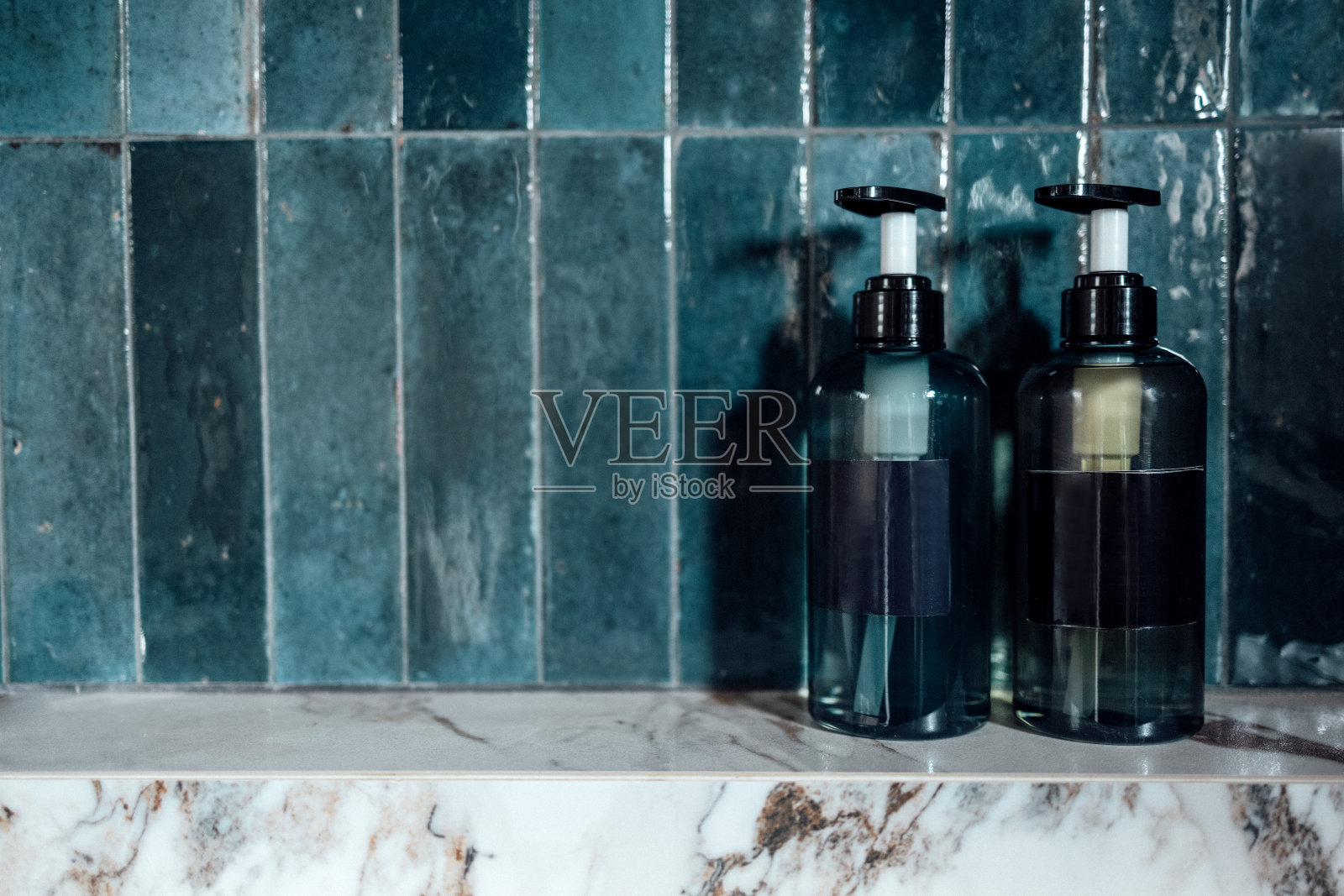 浴室里的蓝色塑料瓶和分配器的特写布局。洗发水或凝胶管的模型，在瓷砖的背景上有黑色的空标签。照片摄影图片