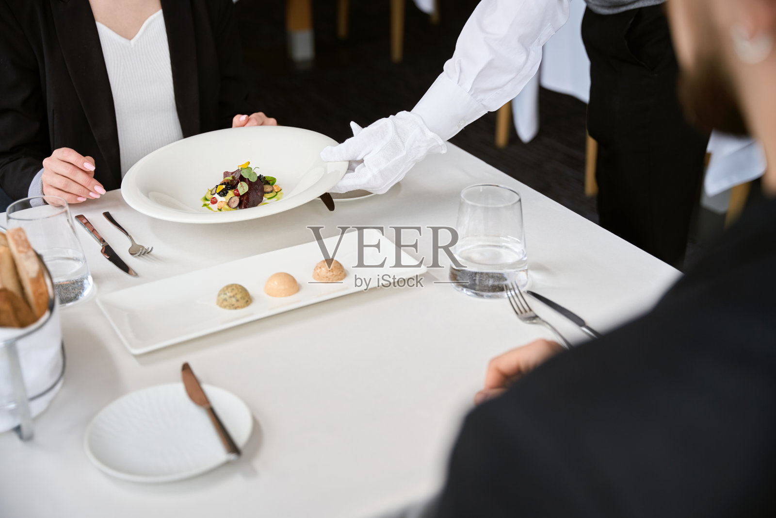 在餐馆里，服务员为女士把一盘沙拉放在桌子上照片摄影图片