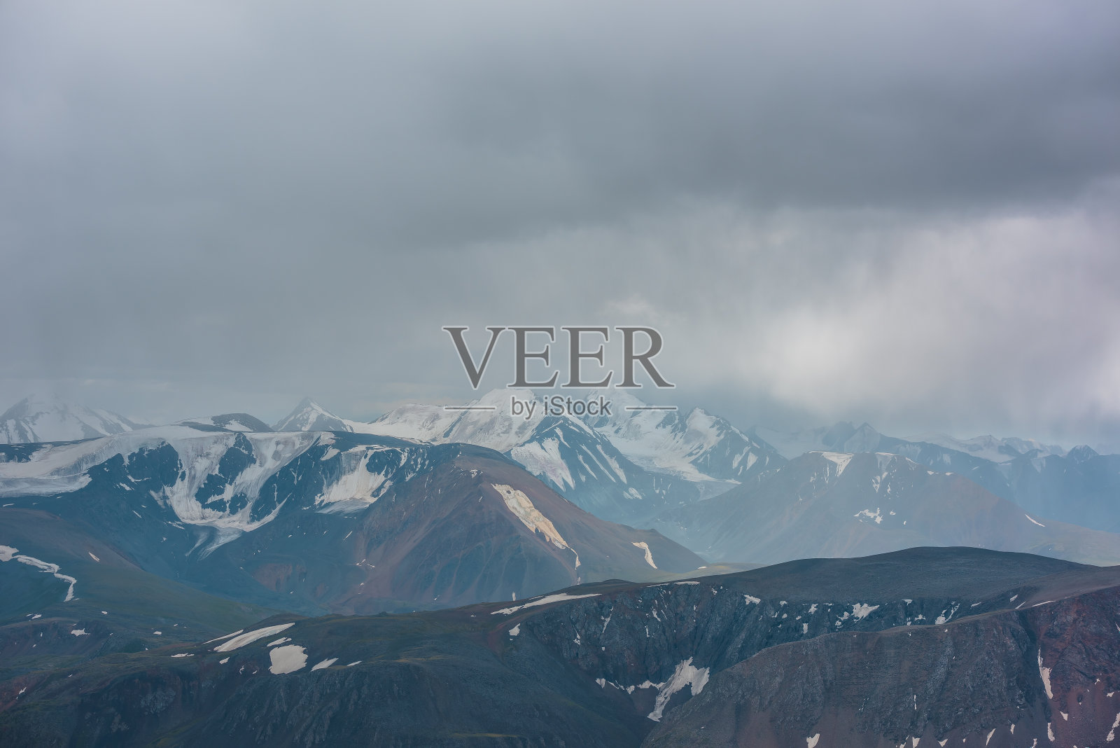 黑暗大气景观与山的轮廓和大积雪覆盖的高峰顶在阴雨低云。在灰色多云的天空中，戏剧性的高山景观。雨中的大雪山。照片摄影图片