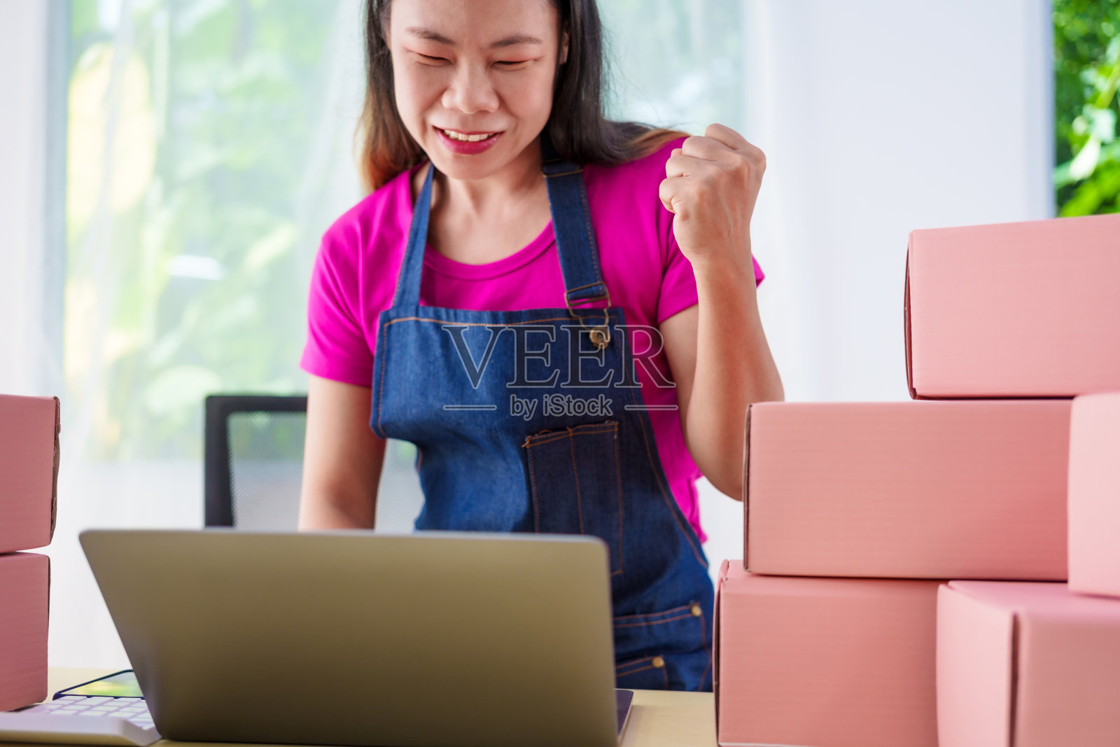 一个穿着工作服的女人在网上销售产品，检查包裹，接受客户订单，在办公桌前工作，用粉红色的盒子包装物品，准备运送给客户。照片摄影图片