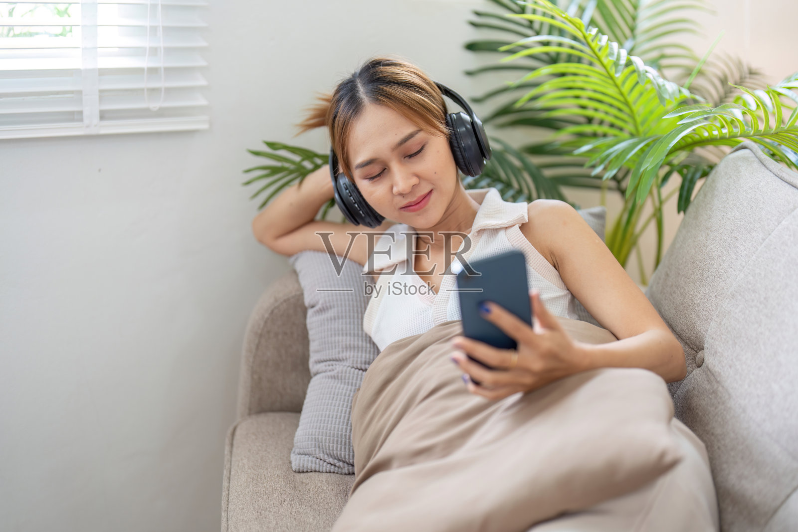 年轻女人在舒适的客厅里戴着耳机和智能手机在沙发上放松照片摄影图片