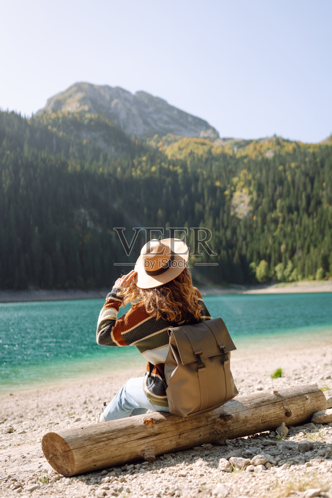 背背包的年轻女子在阳光明媚的天气里看着山上的湖。照片摄影图片