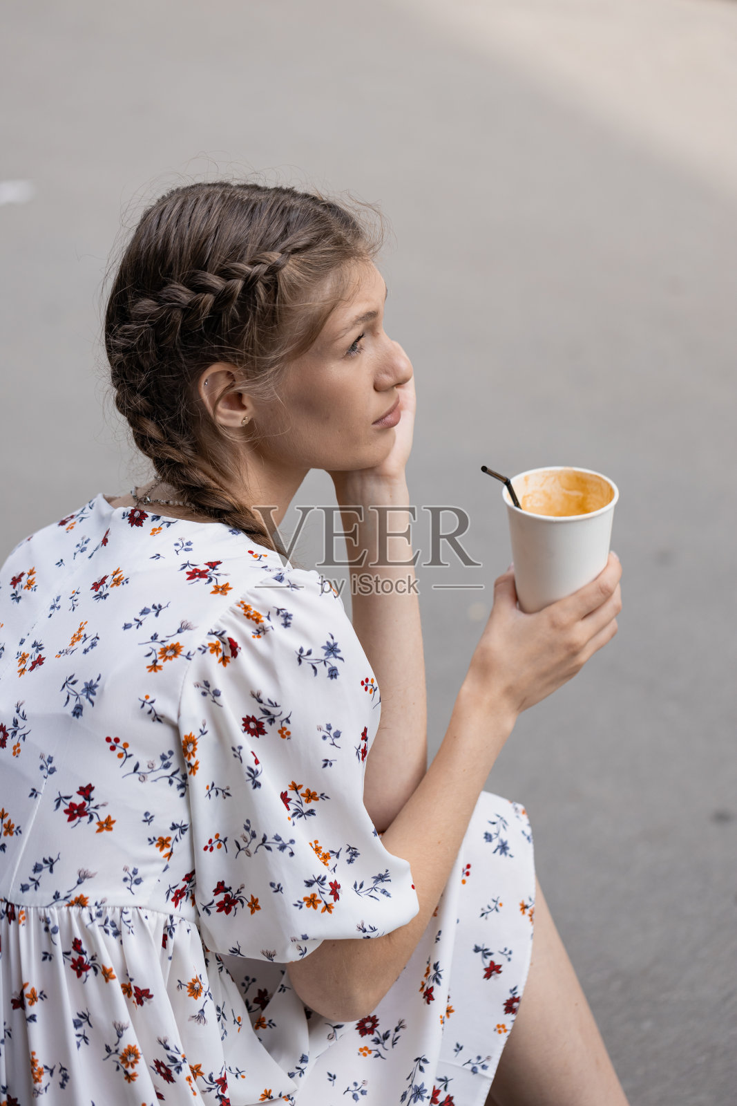 一个年轻的女孩在一个夏日阳光灿烂的日子里在城市的街道上若有所思地喝着咖啡照片摄影图片