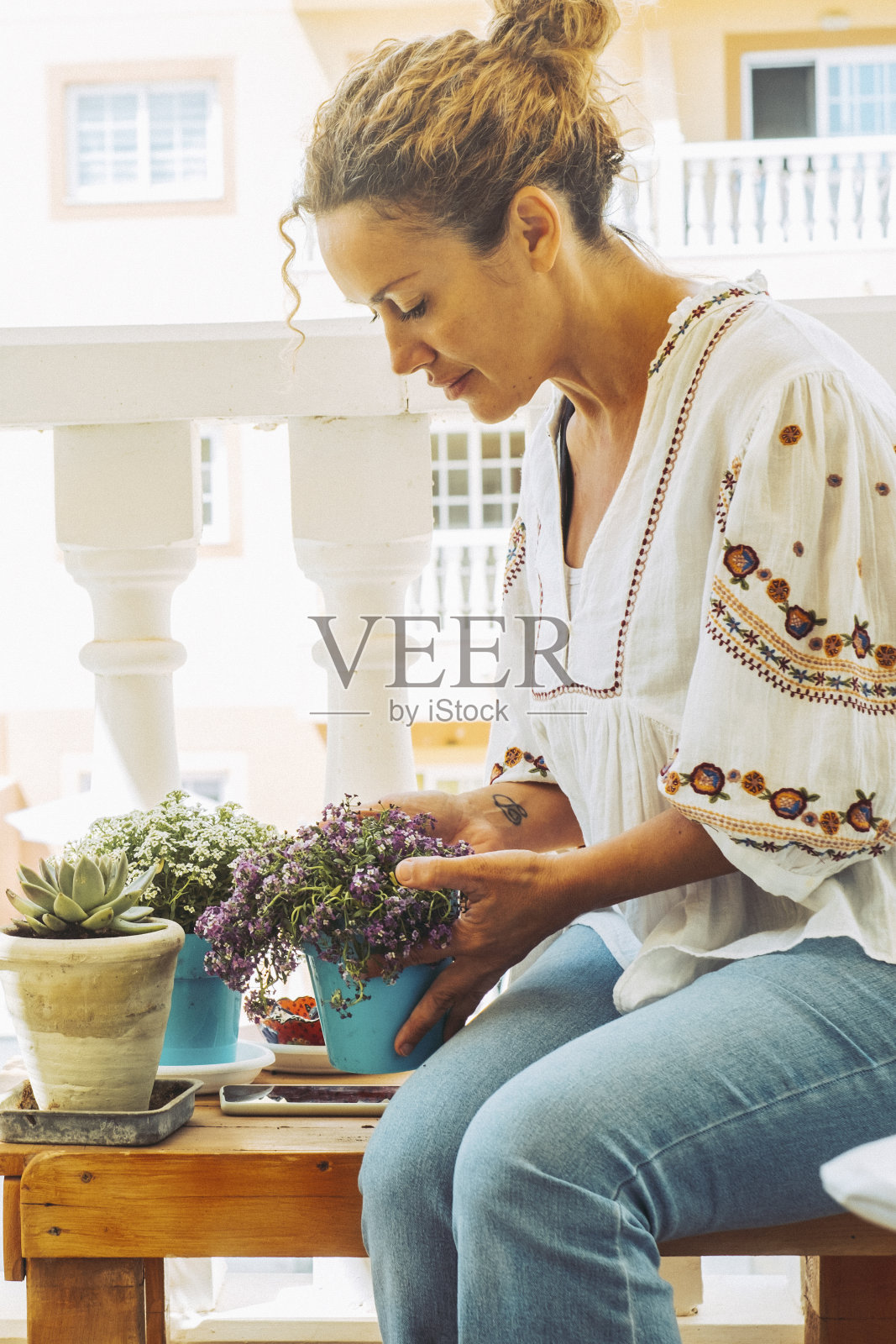 美丽的女士在阳台上照顾她的植物。坐着的金发女郎欣赏着她的花。爱好与植物护理理念照片摄影图片