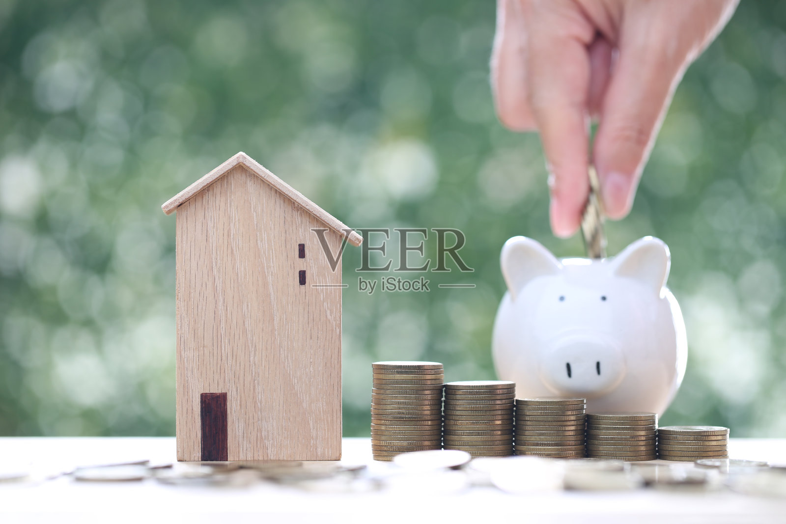 以自然绿色为背景，以储钱罐和一叠硬币为图案的样板房，商业投资和房地产概念照片摄影图片