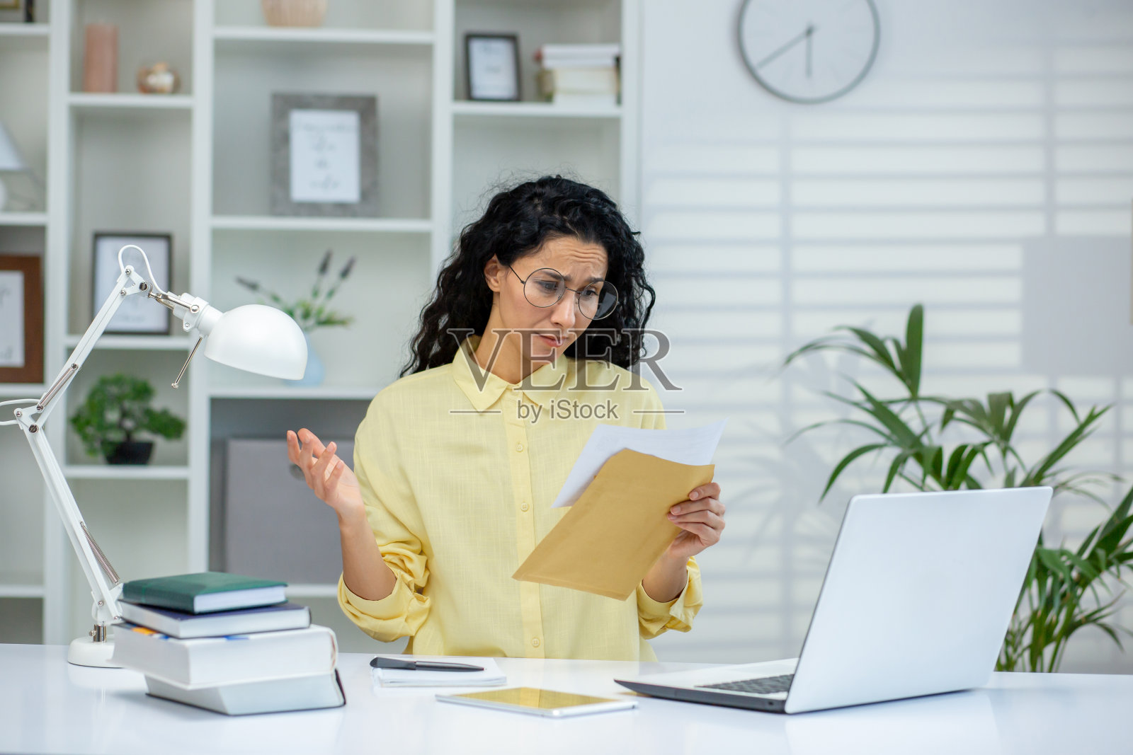 一名女子在家庭办公室的办公桌前阅读文件时看起来很担心照片摄影图片