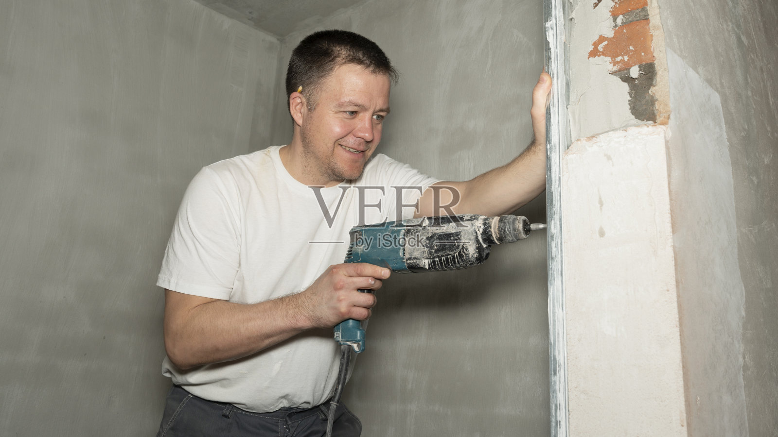 年轻的建筑工人正在墙上钻孔照片摄影图片