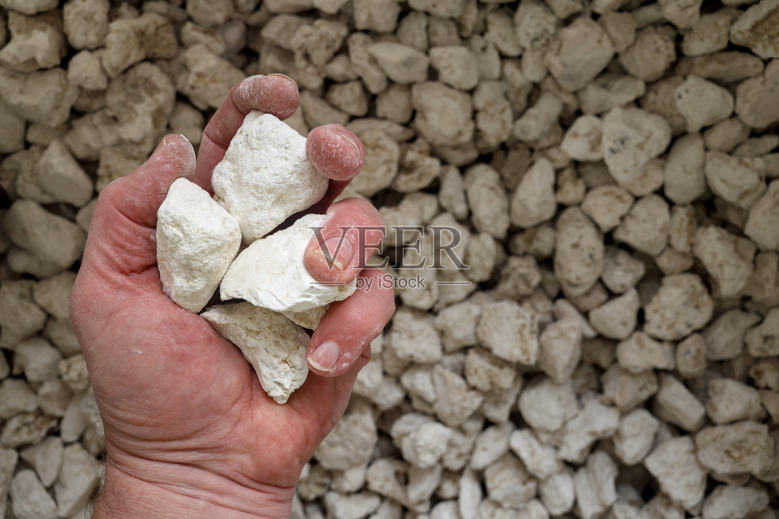 菱镁矿(碳酸镁，MgCO3)矿石，工业矿物，镁(Mg)源。开采于俄罗斯、中国、土耳其、巴西、澳大利亚、奥地利、西班牙、斯洛伐克、希腊、沙特阿拉伯。用半闭的手握住的照片摄影图片