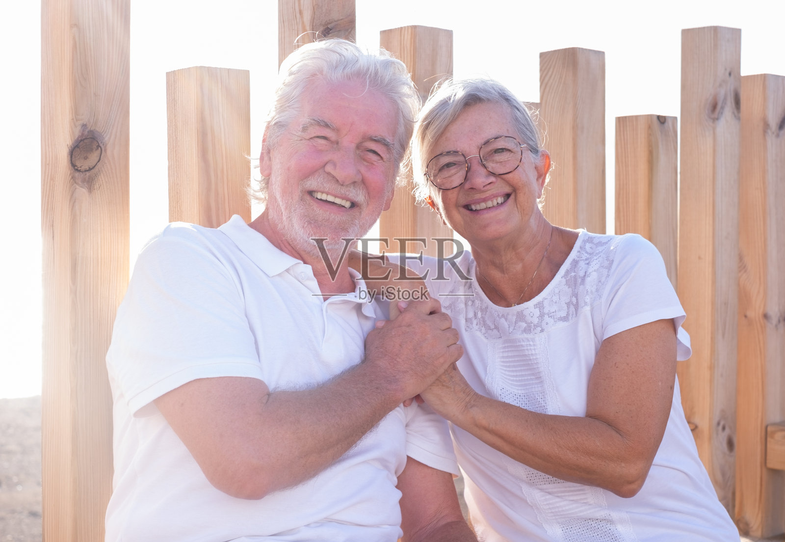 阳光明媚的日子里，一对退休的白人夫妇穿着白色衣服坐在户外，看着镜头，表达着爱和幸福照片摄影图片