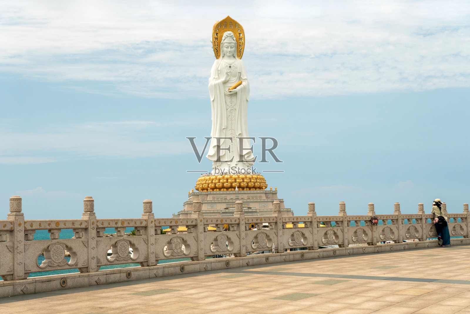 三亚,中国。在南山寺，一名游客带着雨伞在一尊巨大的南海观音雕像前给女孩拍照照片摄影图片