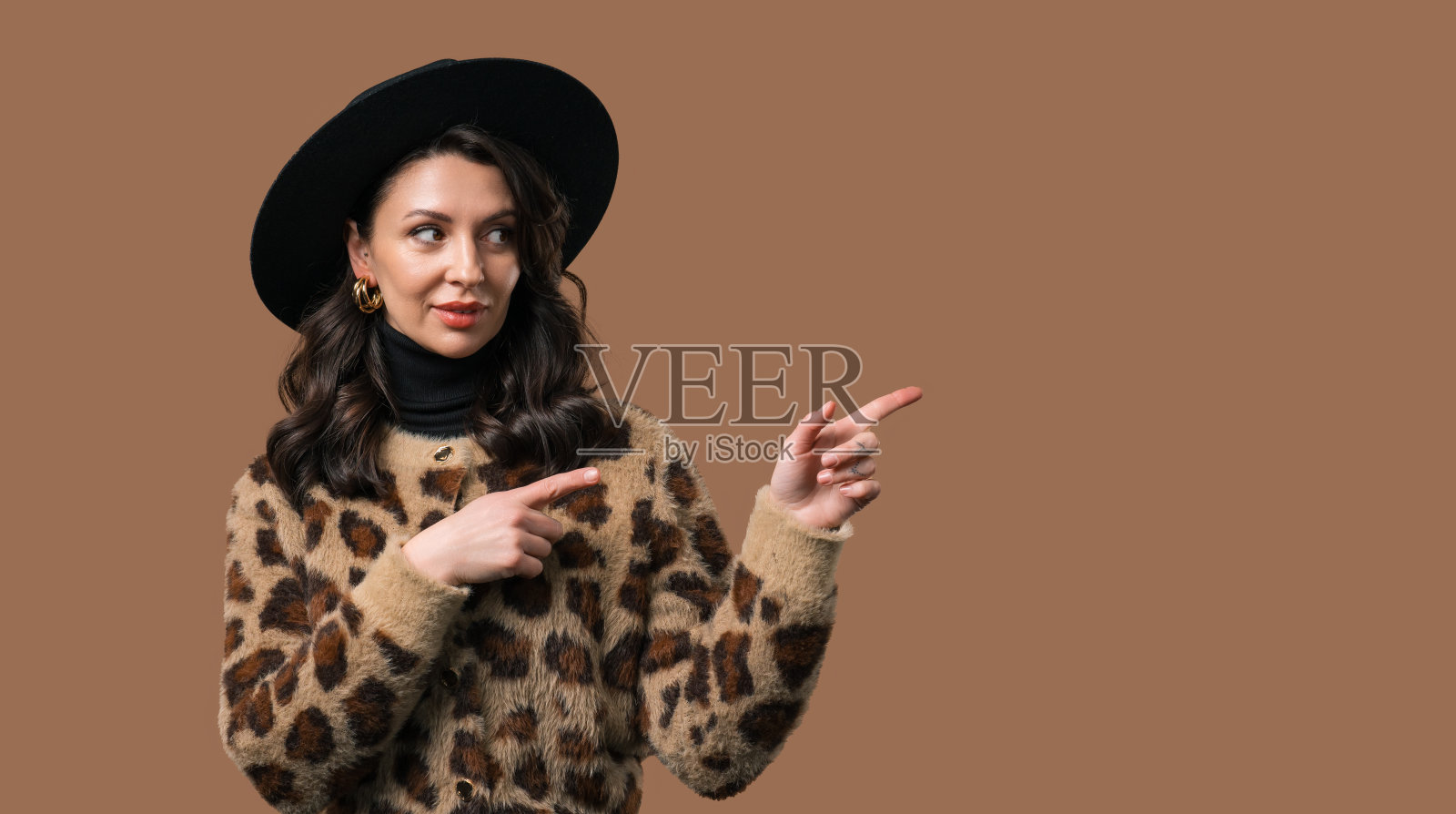 快乐的推广女人呈现在工作空间，模型，推广商业孤立的米色背景。的时尚女士的肖像，用手臂指着左边的复制空间。照片摄影图片