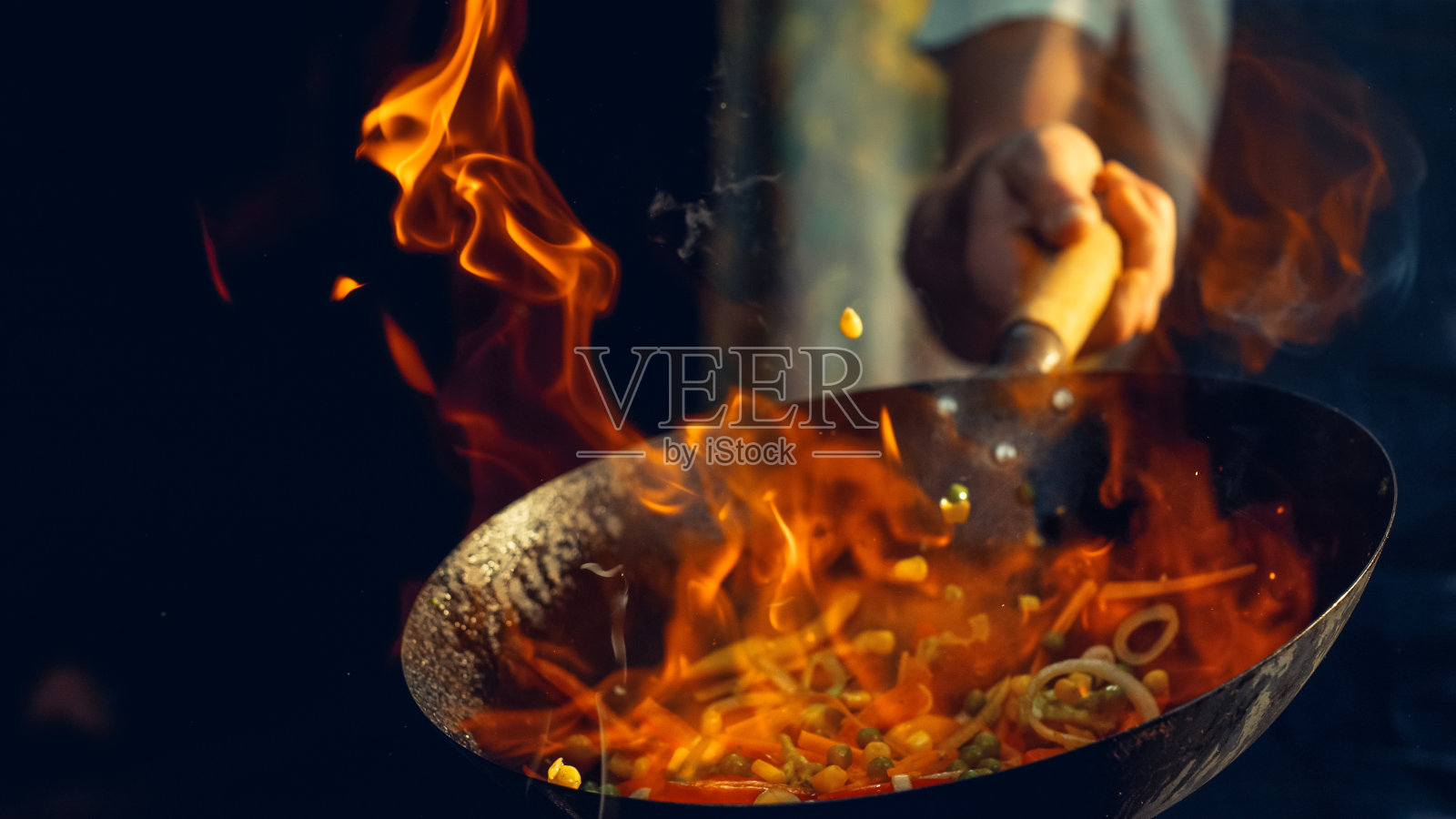 厨师在火焰锅中熟练地煸炒充满活力的蔬菜，在专业的厨房环境中捕捉动态烹饪和新鲜食材的精髓，突出烹饪专业知识照片摄影图片