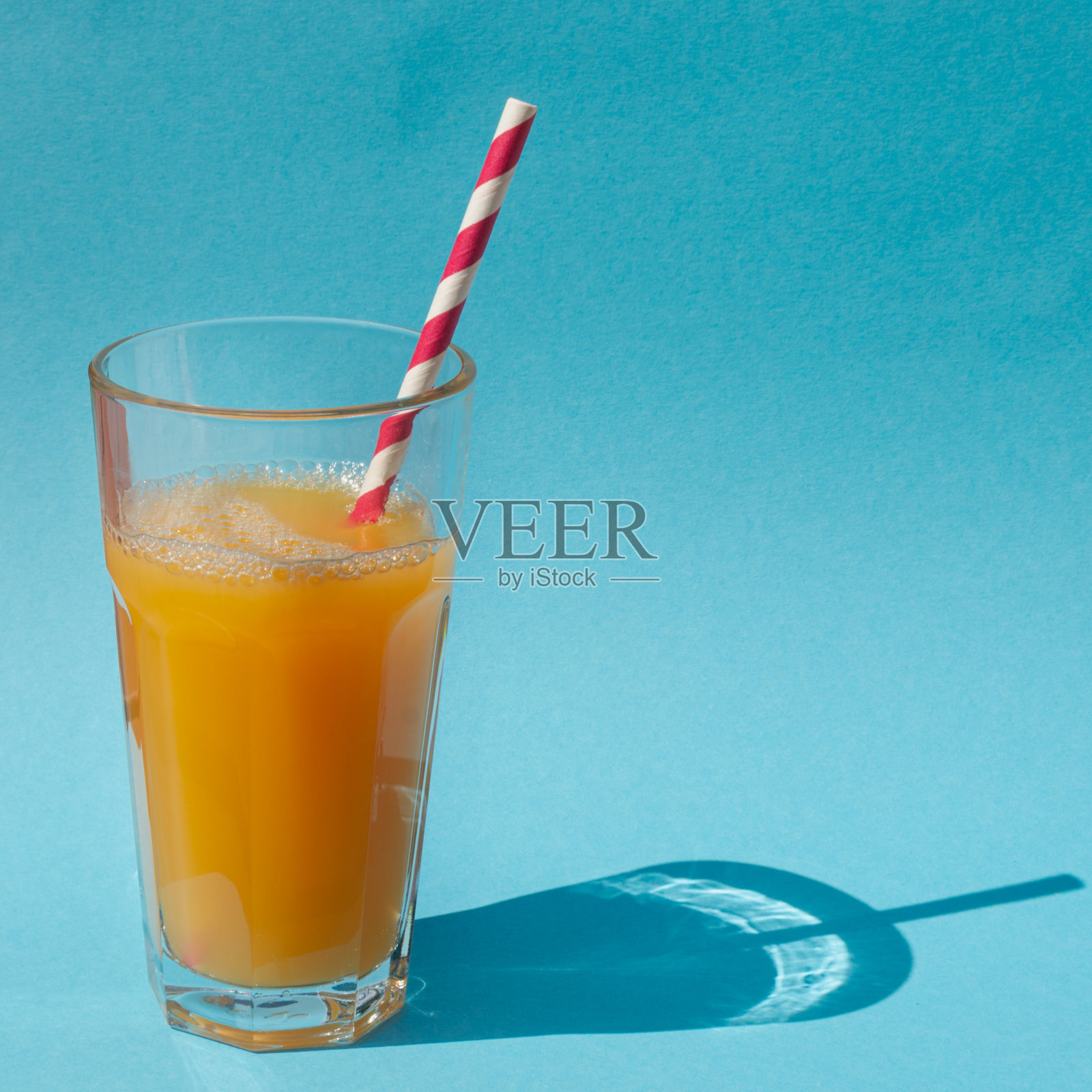 用橙汁或南瓜汁和稻草做成的玻璃杯，蓝色的背景上有太阳的影子照片摄影图片