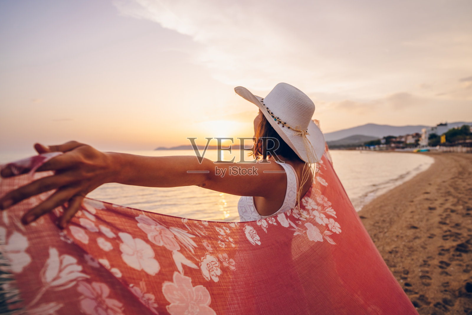 一个女人在海边欣赏日落，伸着胳膊，拿着围巾照片摄影图片