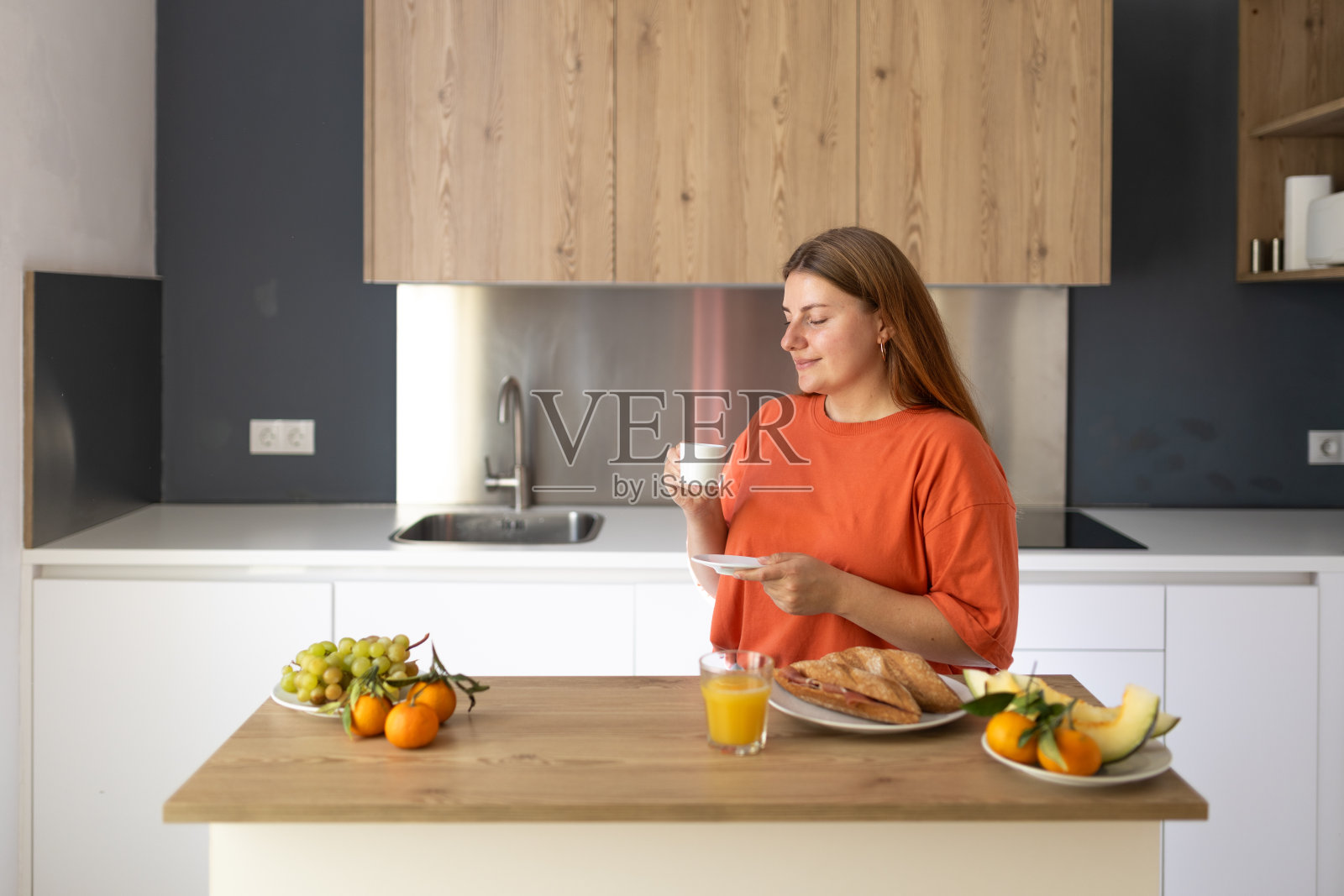 悠闲随意的年轻美丽的快乐微笑的女人在慵懒的早晨在舒适的家里喝咖啡。年轻女子在现代化的厨房里享受着新鲜芳香的咖啡照片摄影图片