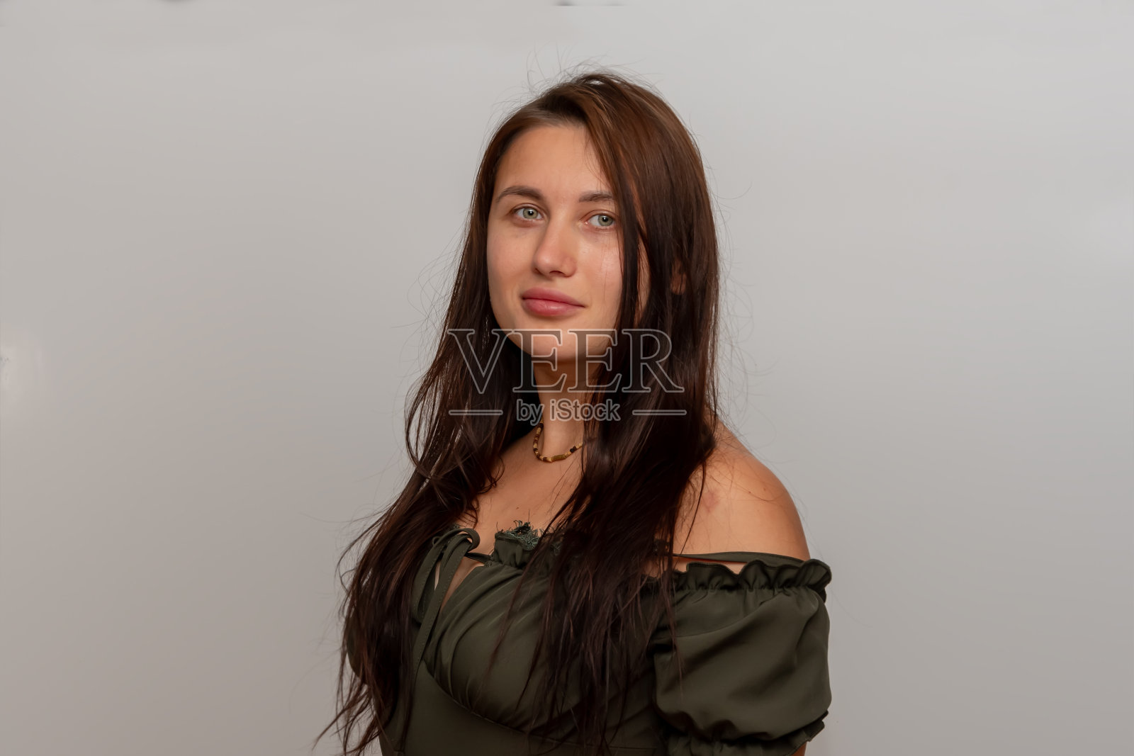 一个棕色长发的女人在浅色背景下穿着绿色连衣裙，肩膀敞开照片摄影图片