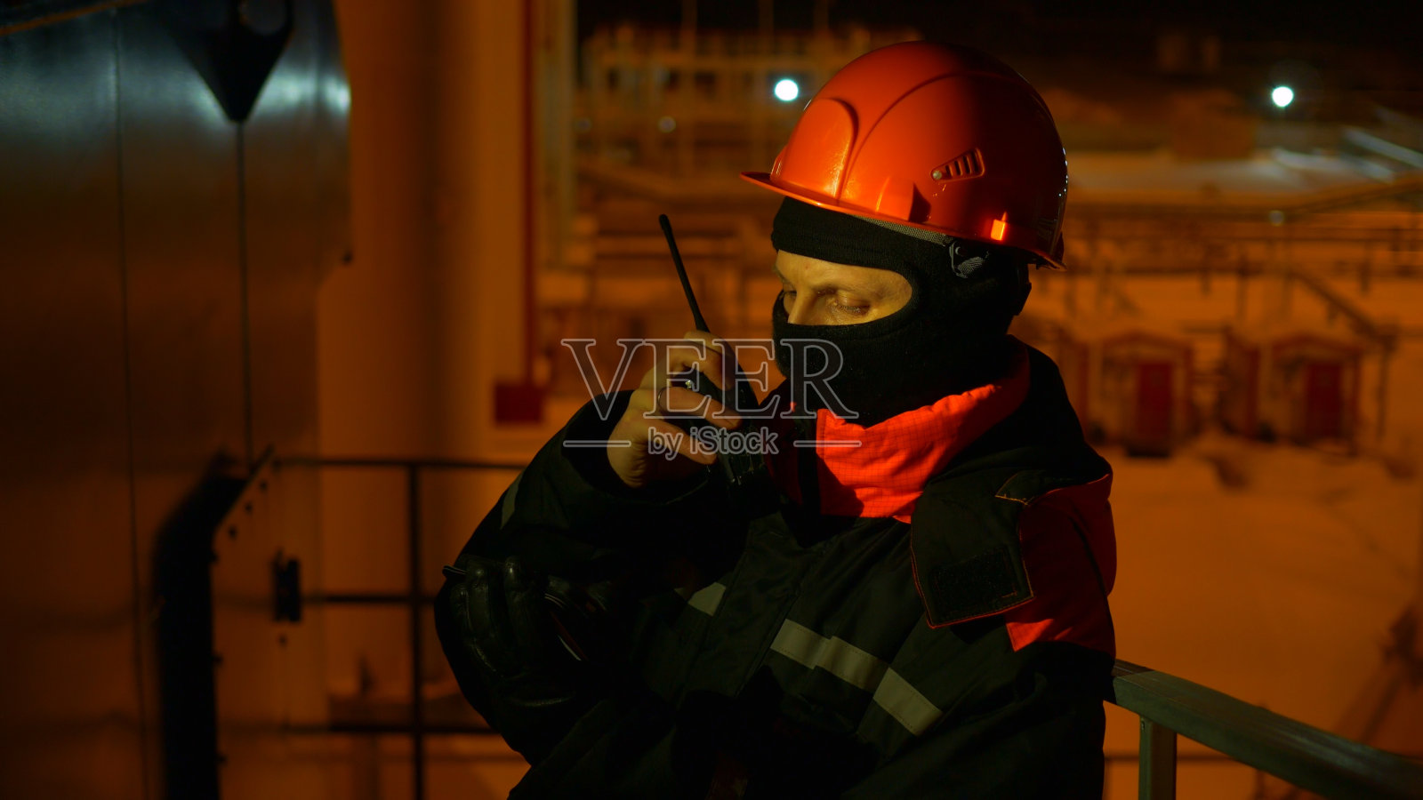 工厂的夜班工程师用无线电与同事沟通。专注，安全为导向的工程师确保在工业环境中顺利运行。高风险环境下的深夜轮班。照片摄影图片