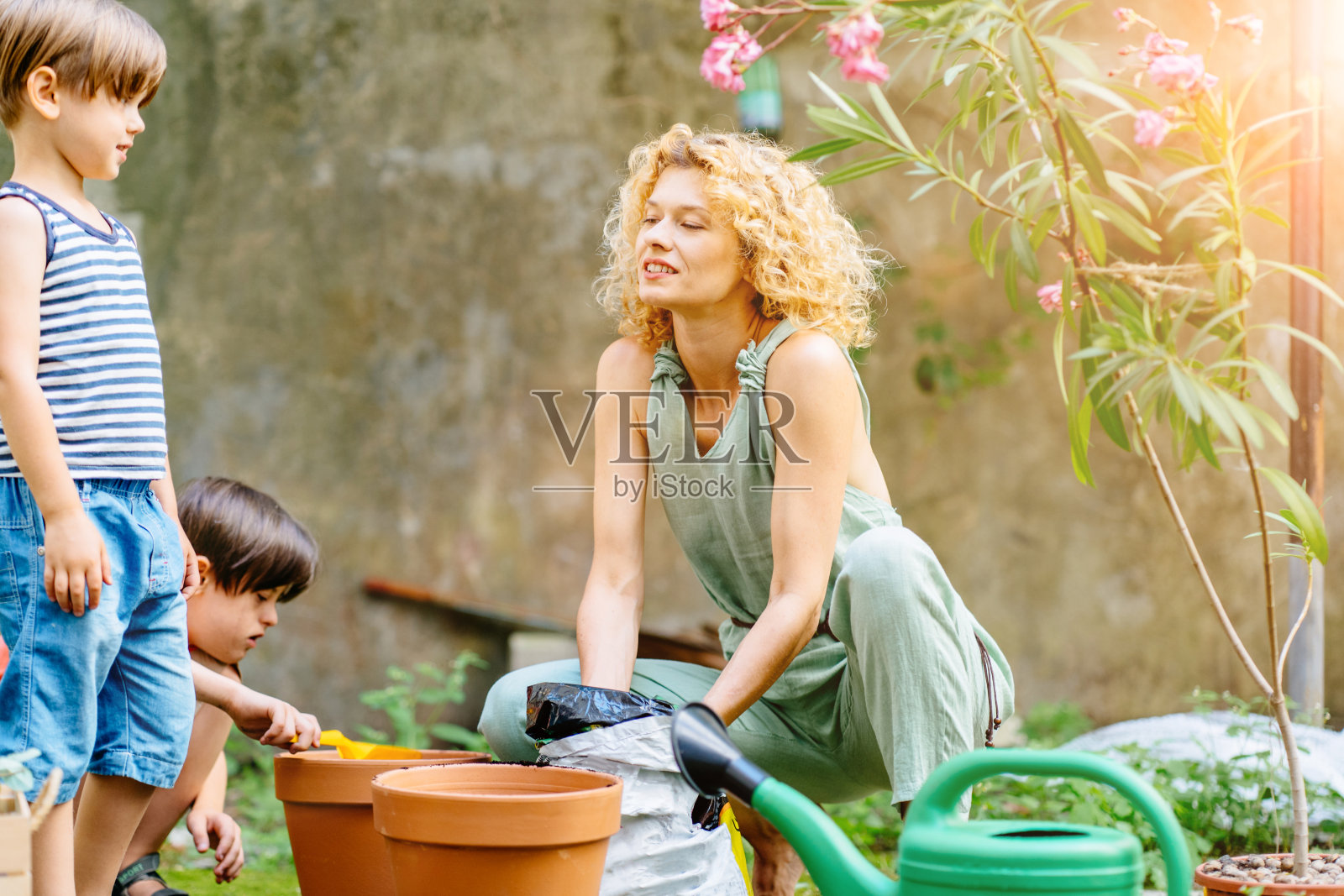 患有唐氏综合征的儿童在花园里和金发母亲（园丁）一起学习种花，母亲戴着黑色手套，在户外花园里和儿子一起工作，充满爱意。照片摄影图片