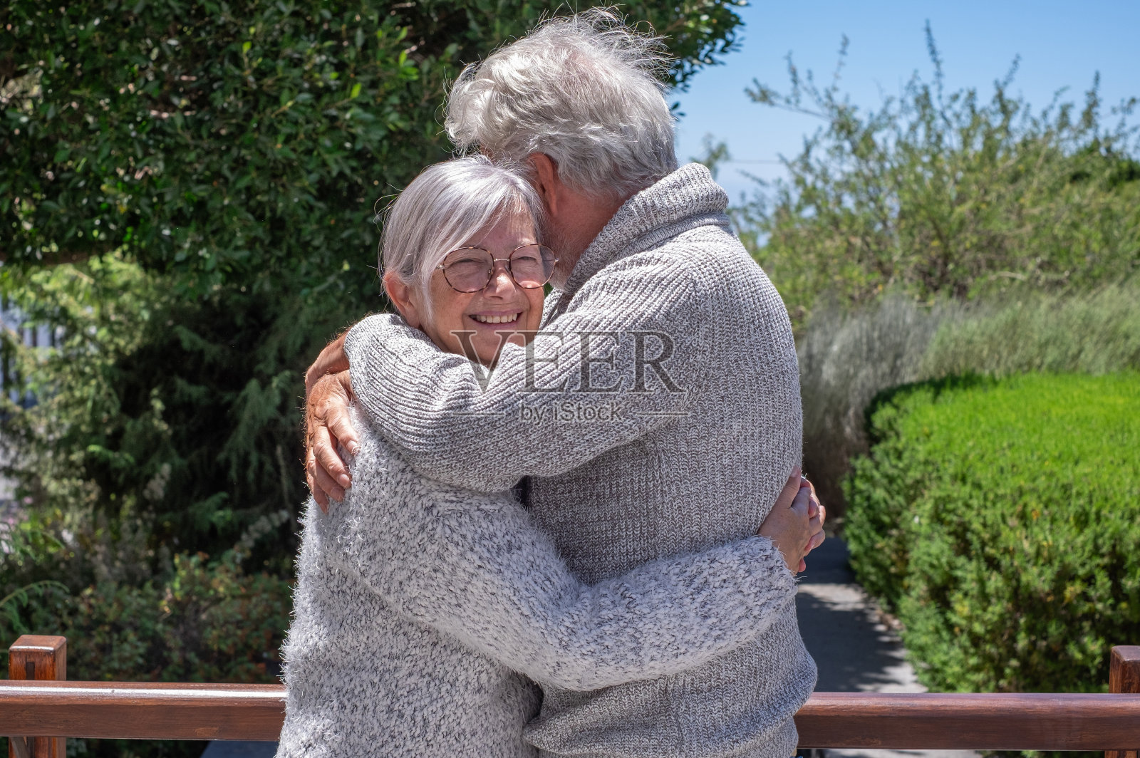 老年夫妇在户外享受美好的一天，微笑着拥抱在一起。退休老人反映了他们深厚的感情。白发苍苍的高加索人在绿色的大自然中快乐照片摄影图片