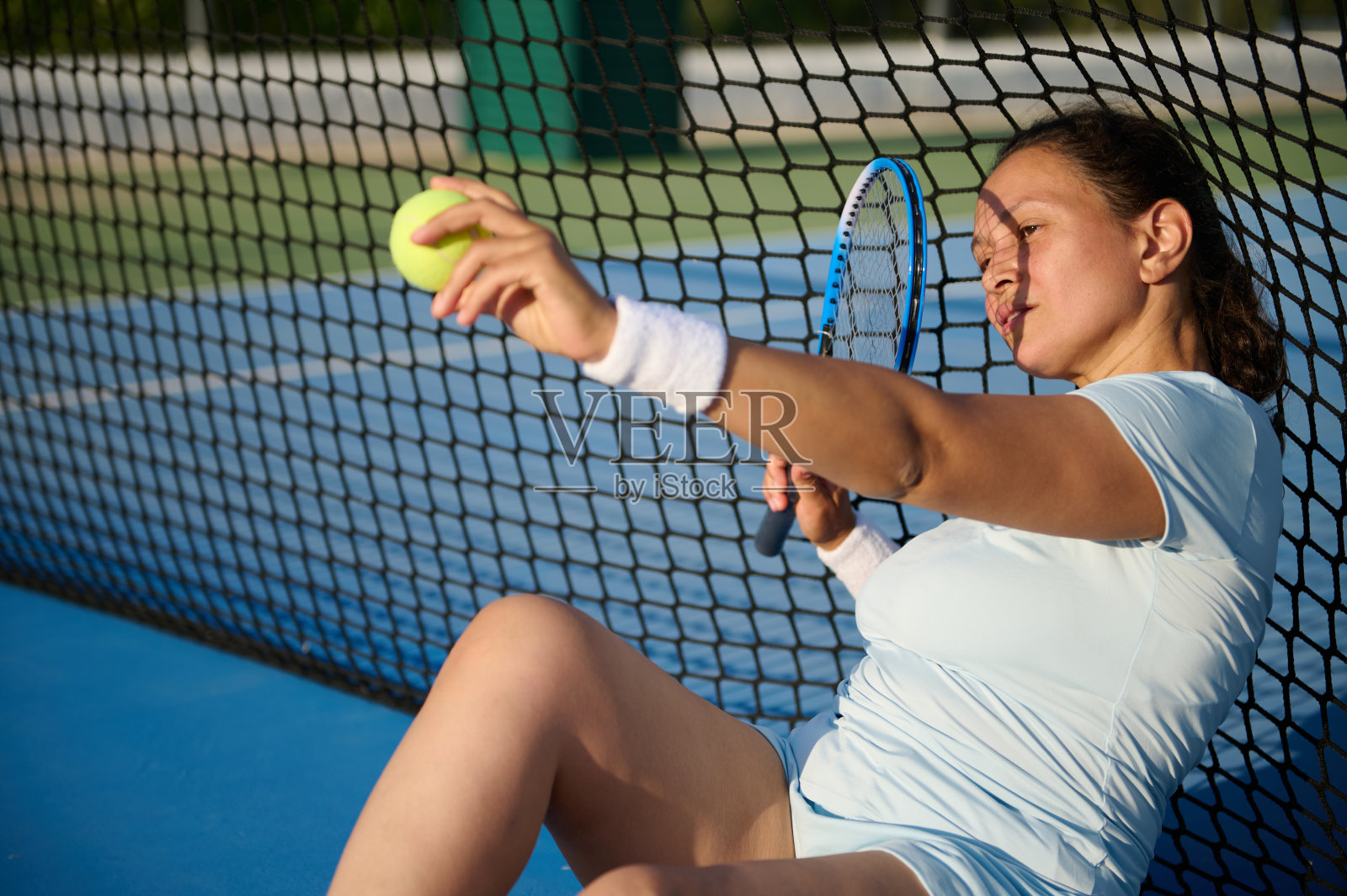 在阳光明媚的球场上，疲惫的网球运动员坐在网旁照片摄影图片