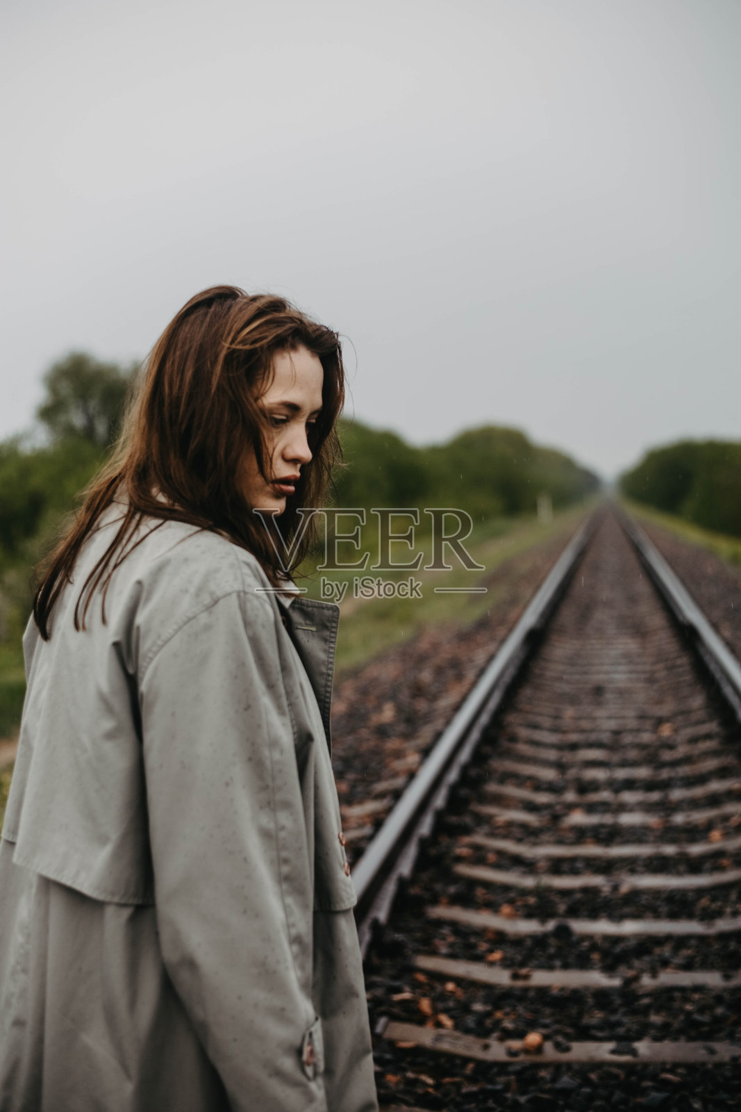 灰色外套的忧郁女人走在铁轨上，危机中的沮丧和悲伤照片摄影图片