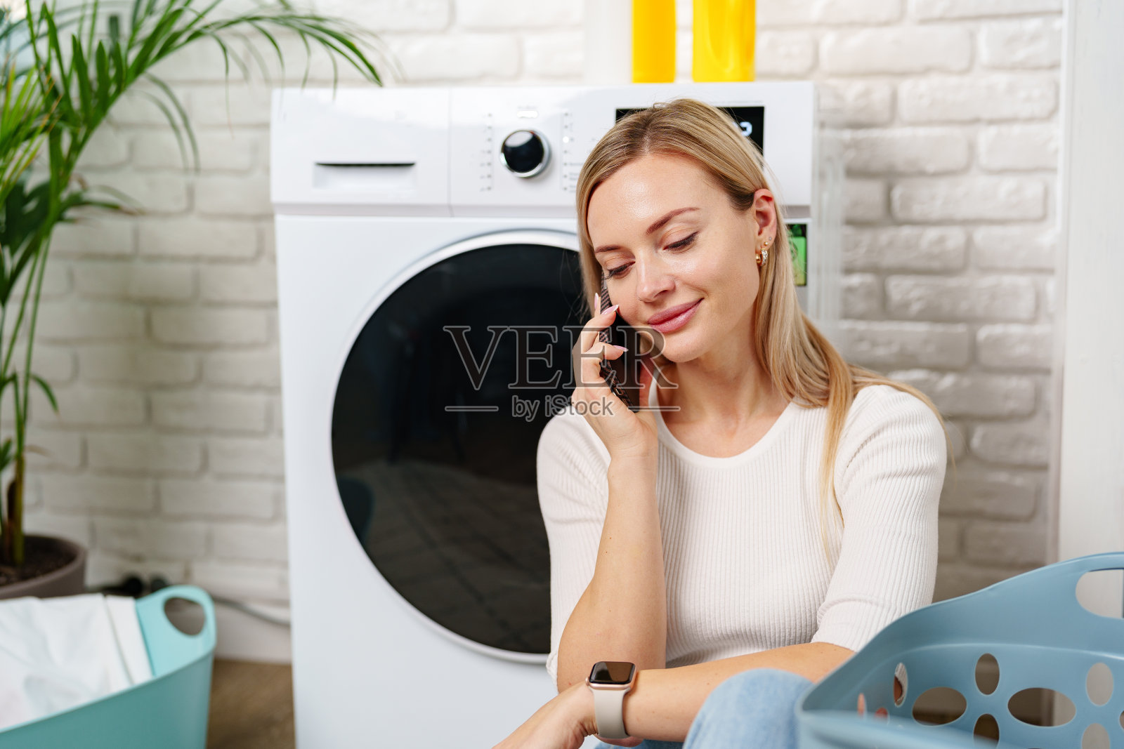 一名女子在洗衣房白色洗衣机旁使用智能手机照片摄影图片