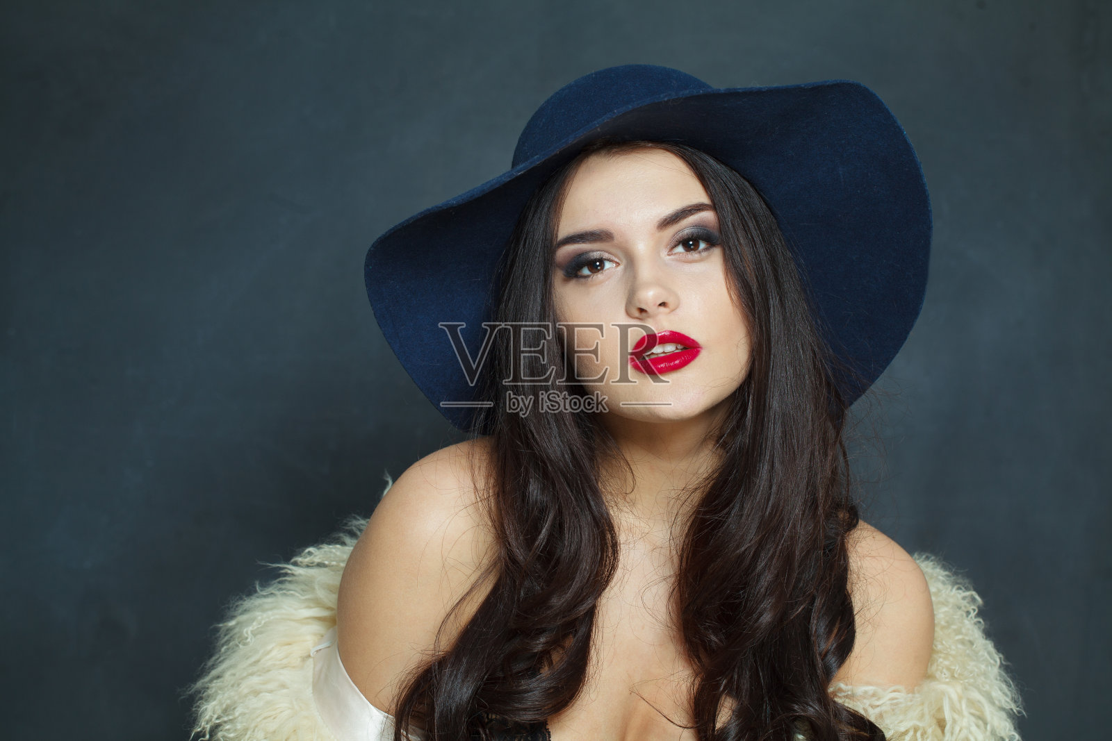 华丽的时尚模特女人长黑色波浪发型和红唇化妆戴时髦的帽子美容工作室肖像照片摄影图片