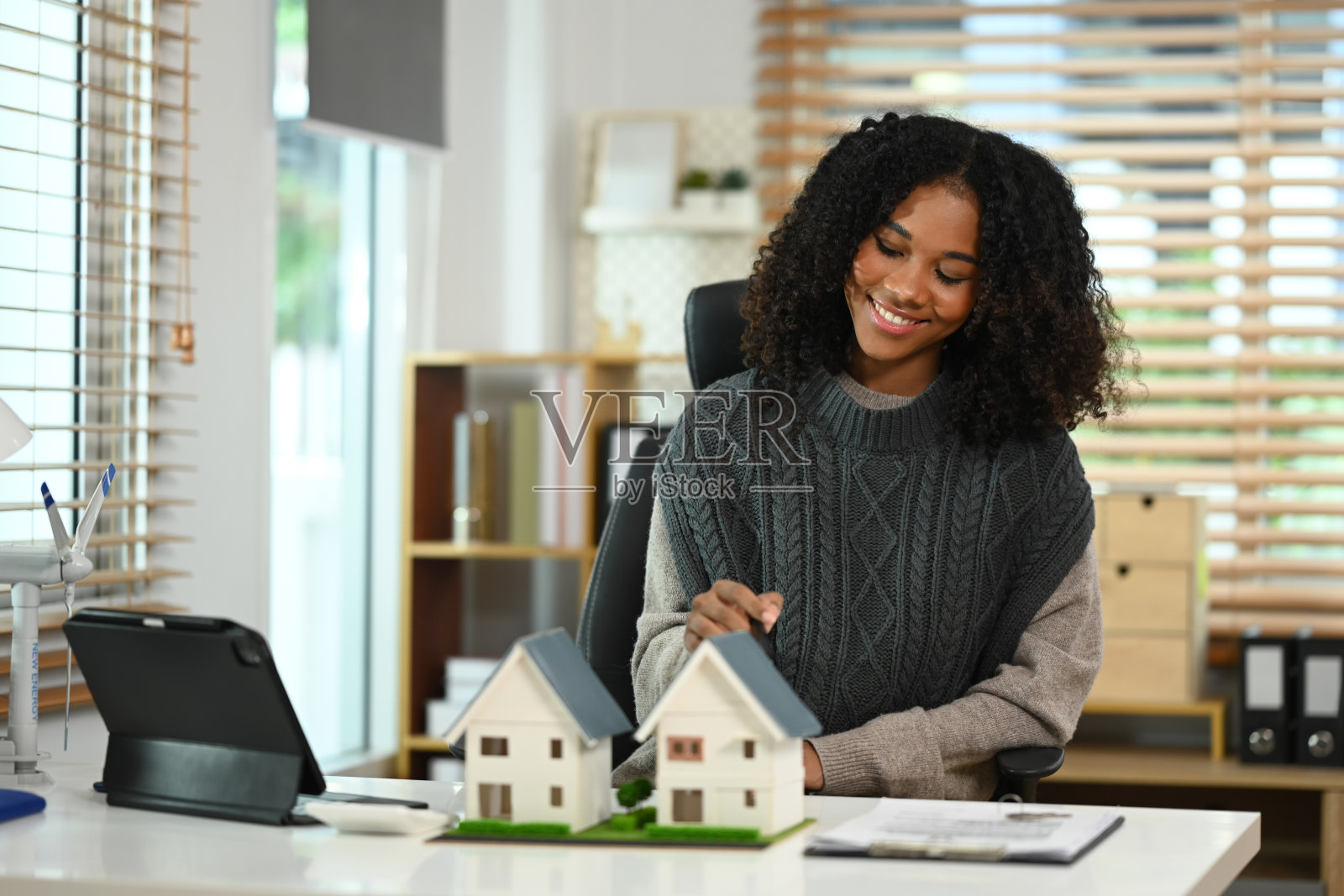 面带微笑的非裔美国妇女手持房屋模型、风力涡轮机、可持续能源和现代科技照片摄影图片