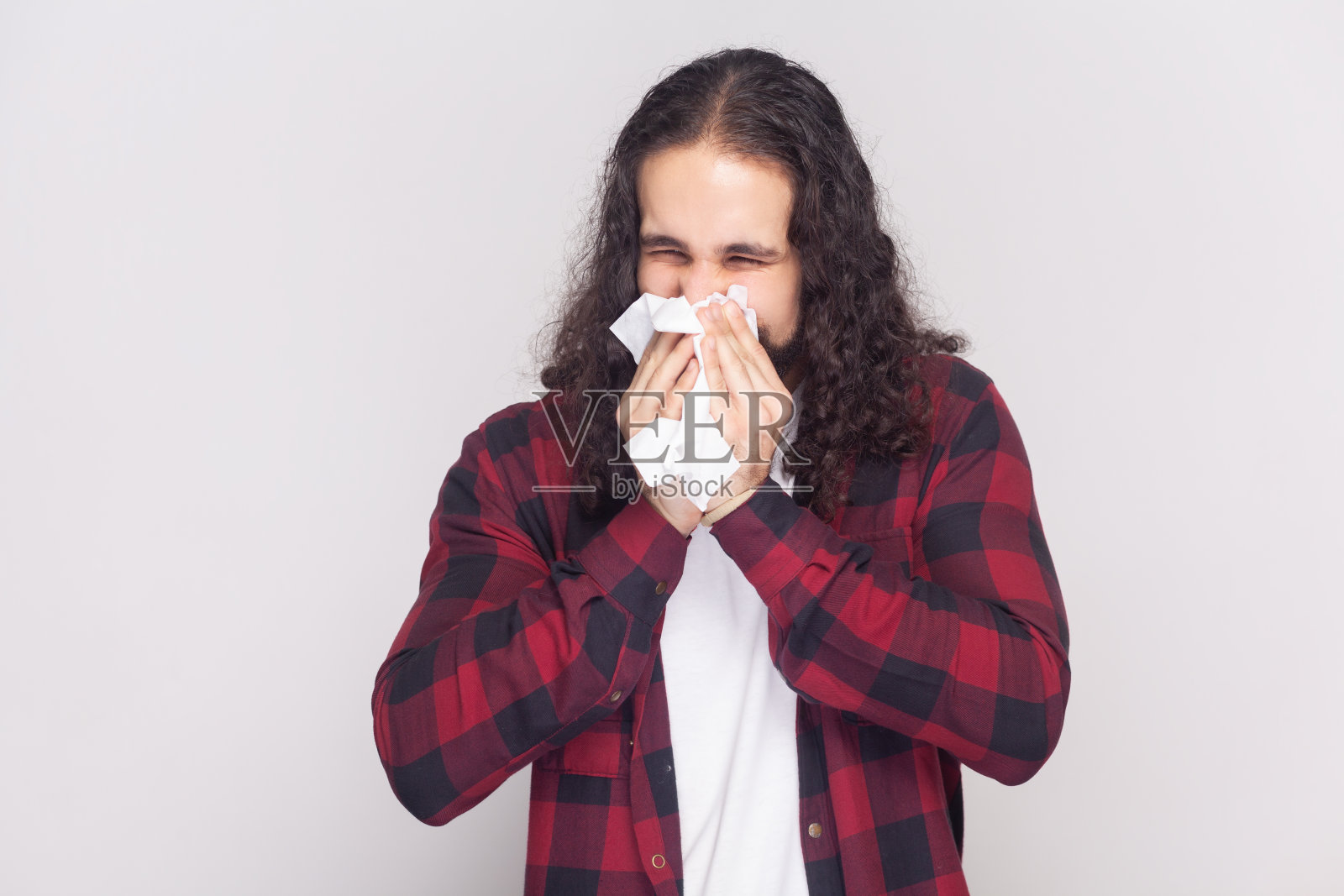 穿着红色格子衬衫的男人用纸巾打喷嚏，患有鼻炎和流鼻涕照片摄影图片