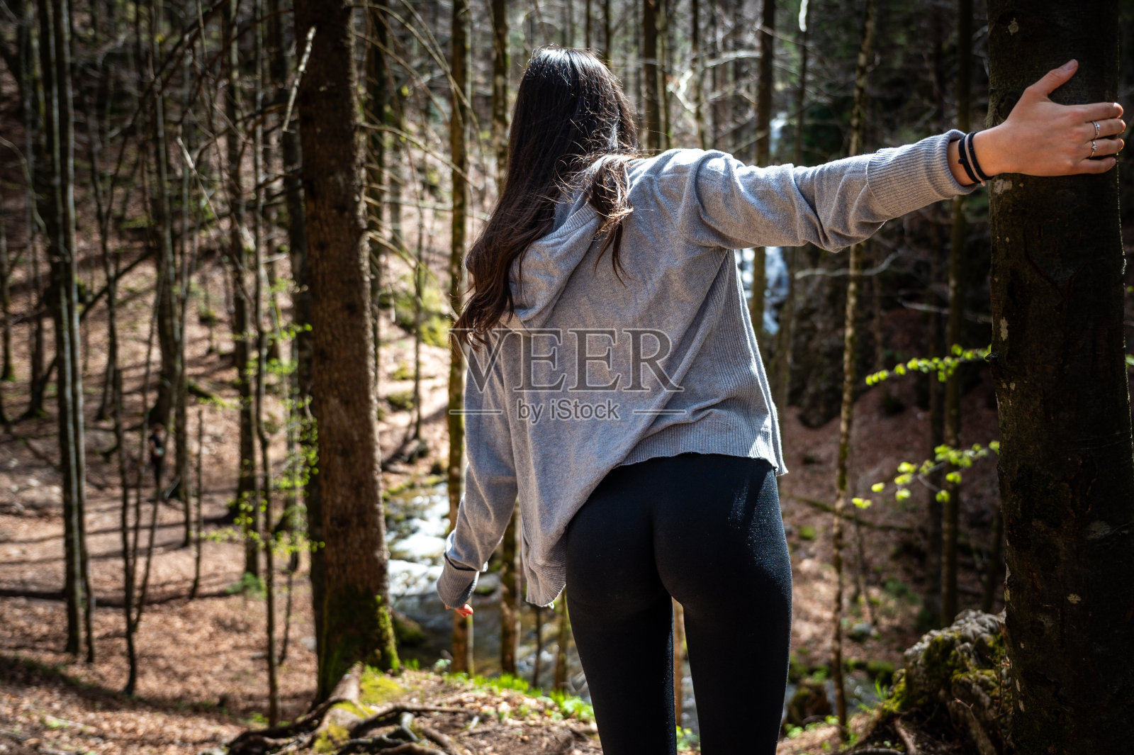 一位年轻女子在树林里抓着一棵树，身体前倾，朝着下山的徒步小径走去照片摄影图片