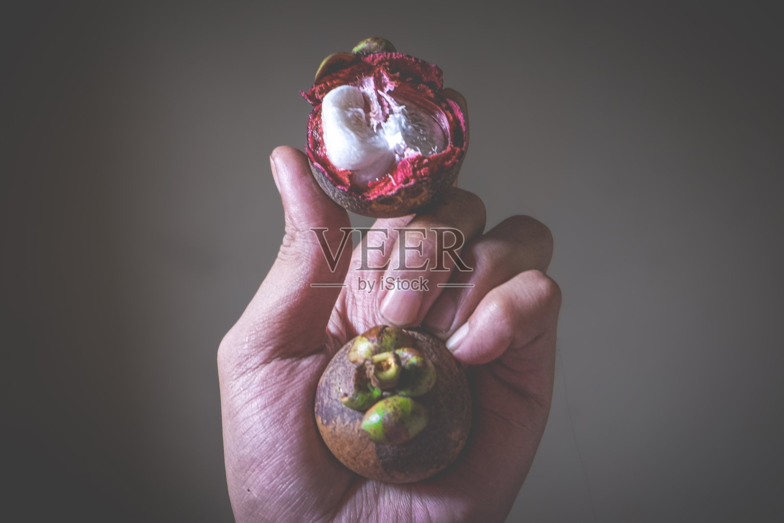 一个女人的手拿着一颗去皮的山竹，一颗裂开的山竹，正在剥山竹照片摄影图片