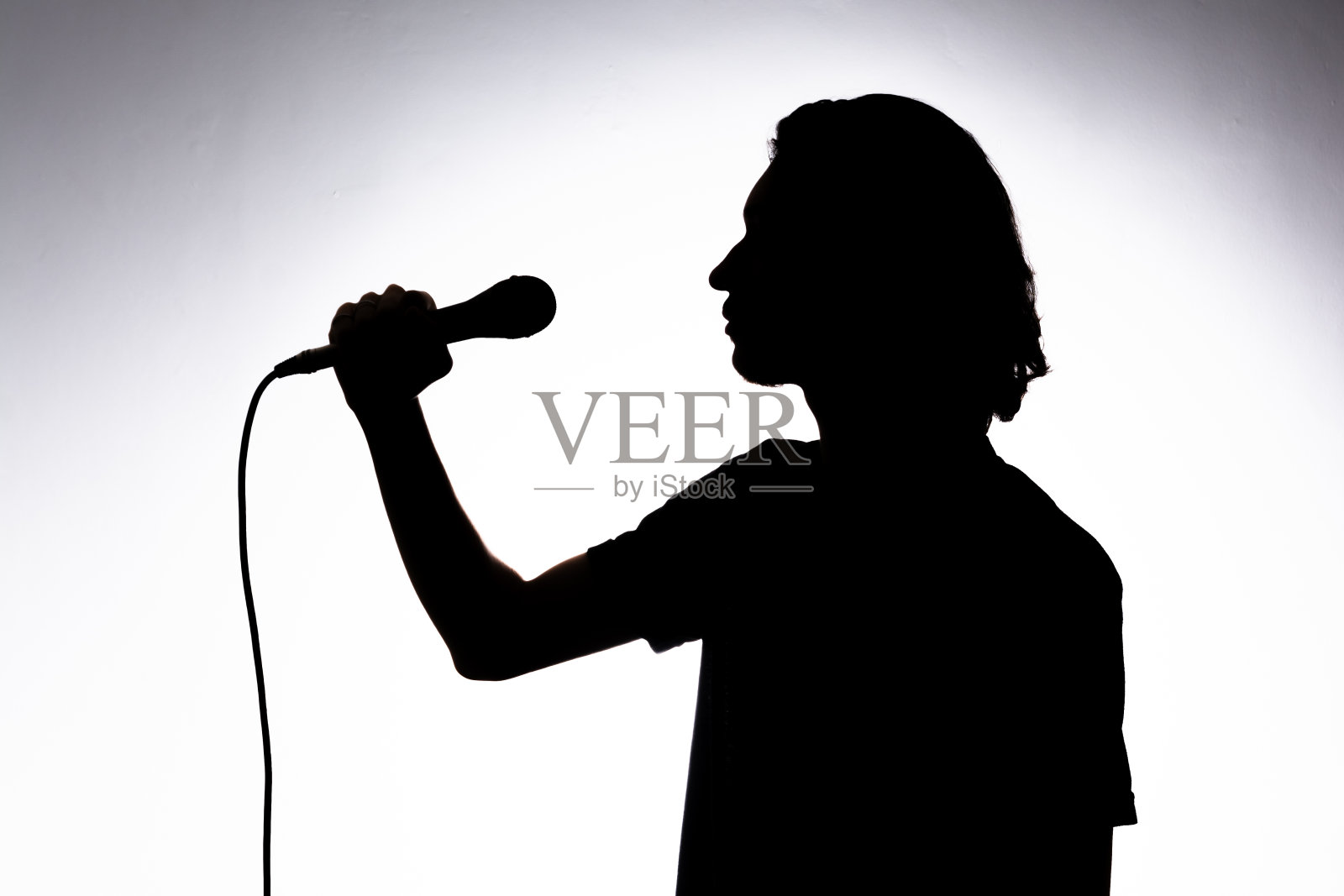 年轻歌手的剪影，手持有线麦克风，动情地歌唱。照片摄影图片