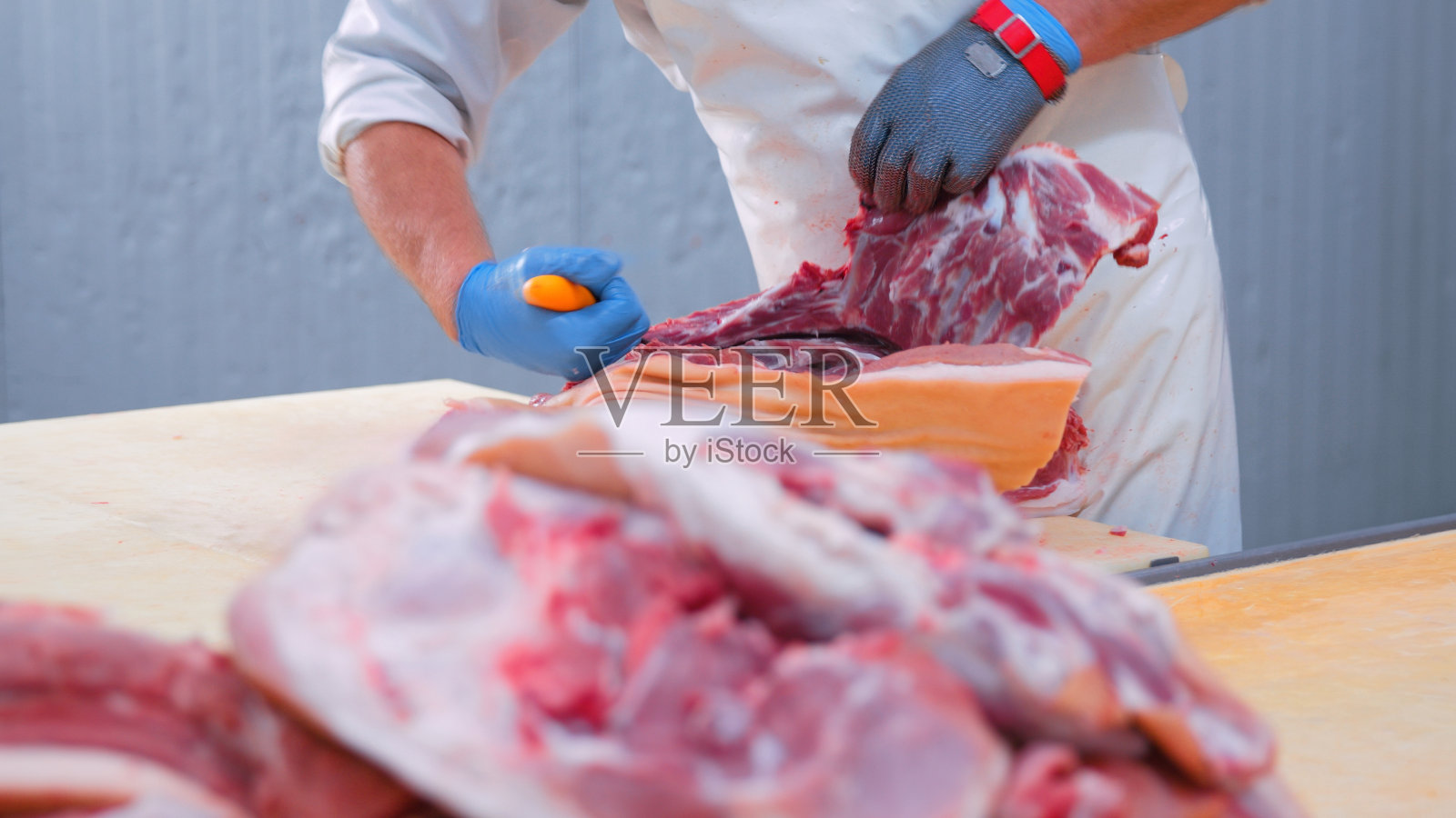 在工业肉制品加工厂，男屠夫正在切猪腿肉照片摄影图片