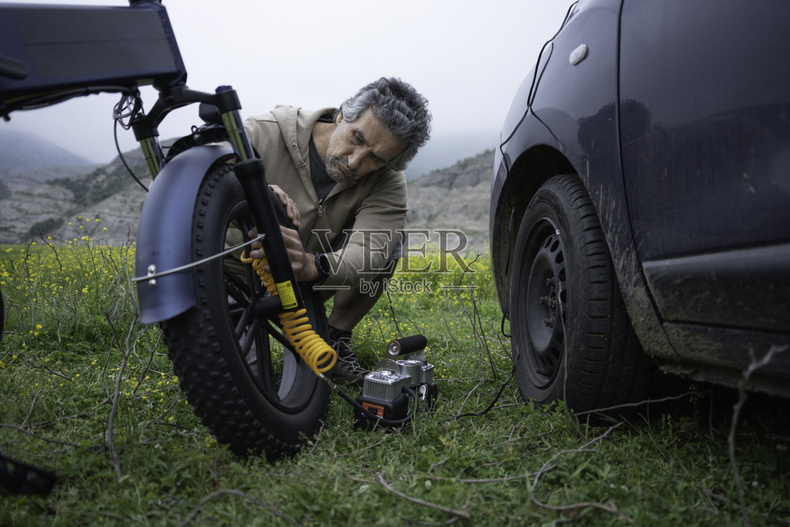 男子用便携式空气压缩机给电动自行车轮胎充气。照片摄影图片