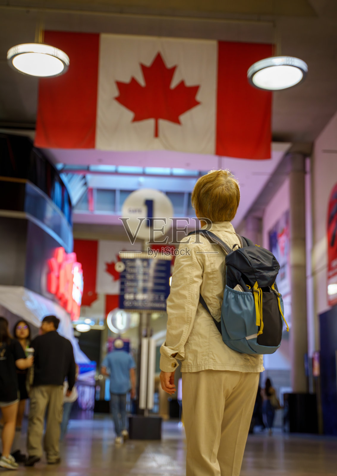 一位年长的女性游客在多伦多联合车站内，背景是加拿大国旗。照片摄影图片