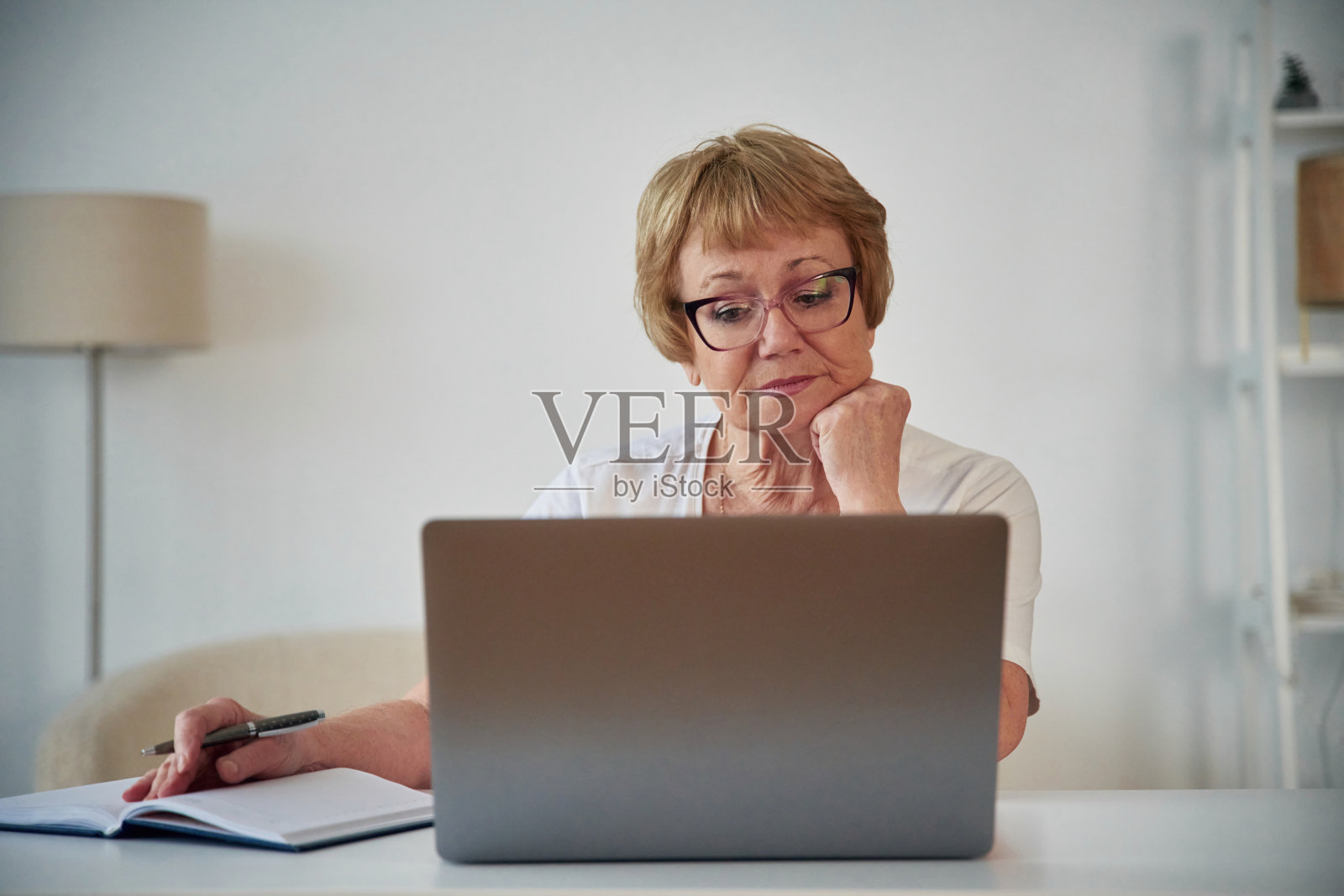 坐在笔记本电脑旁。一位年长的妇女在家里的客厅里照片摄影图片