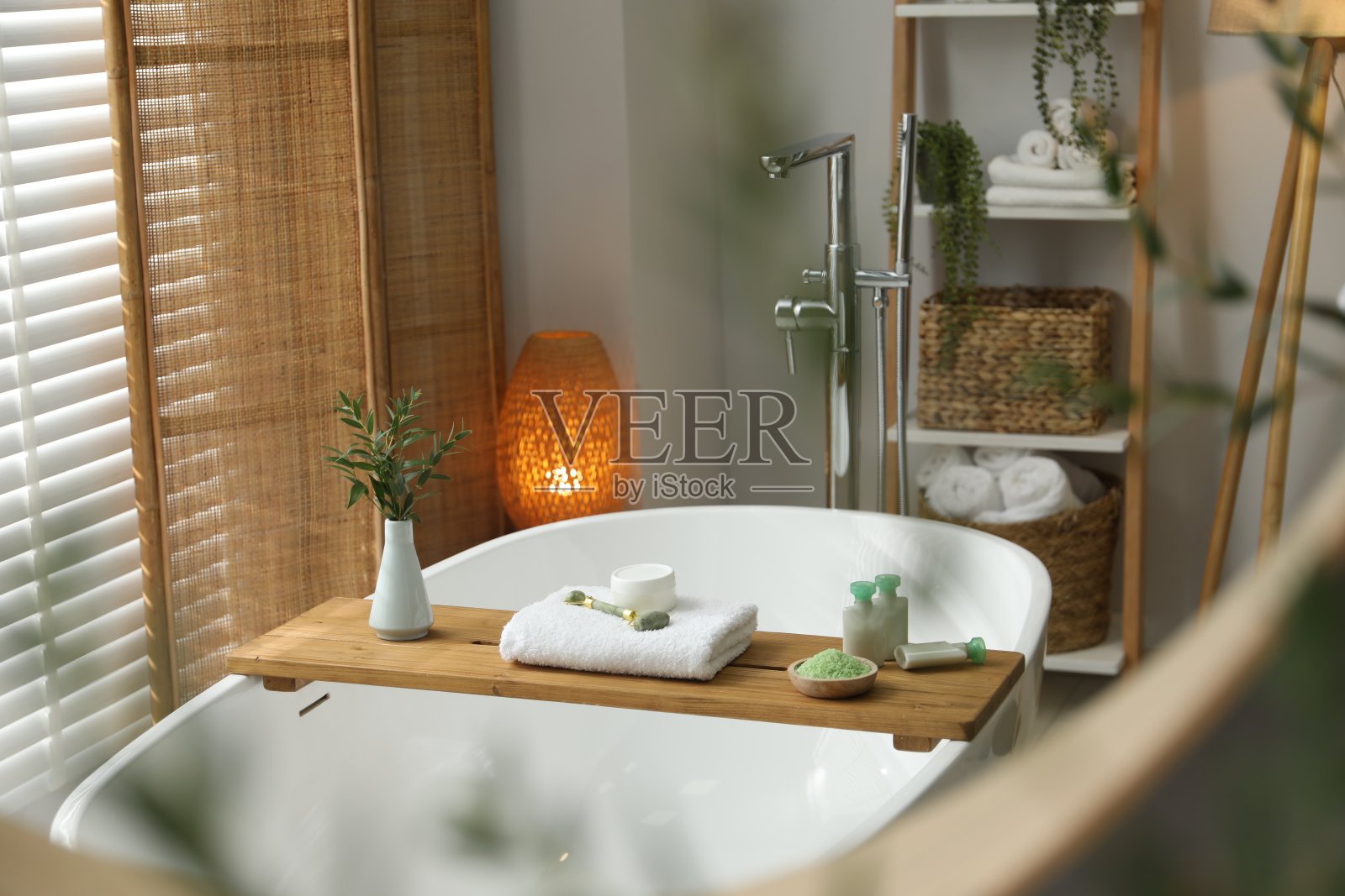 浴室浴缸上的木制托盘上有水疗产品和绿色的树枝，镜子里的倒影照片摄影图片