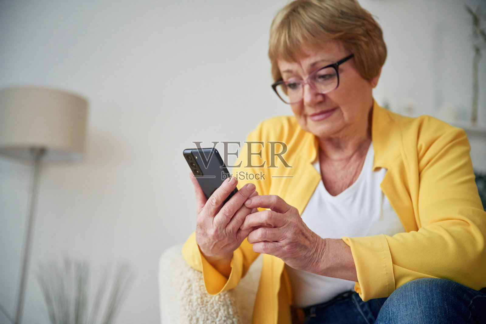 智能手机。一位年长的妇女在家里的客厅里照片摄影图片