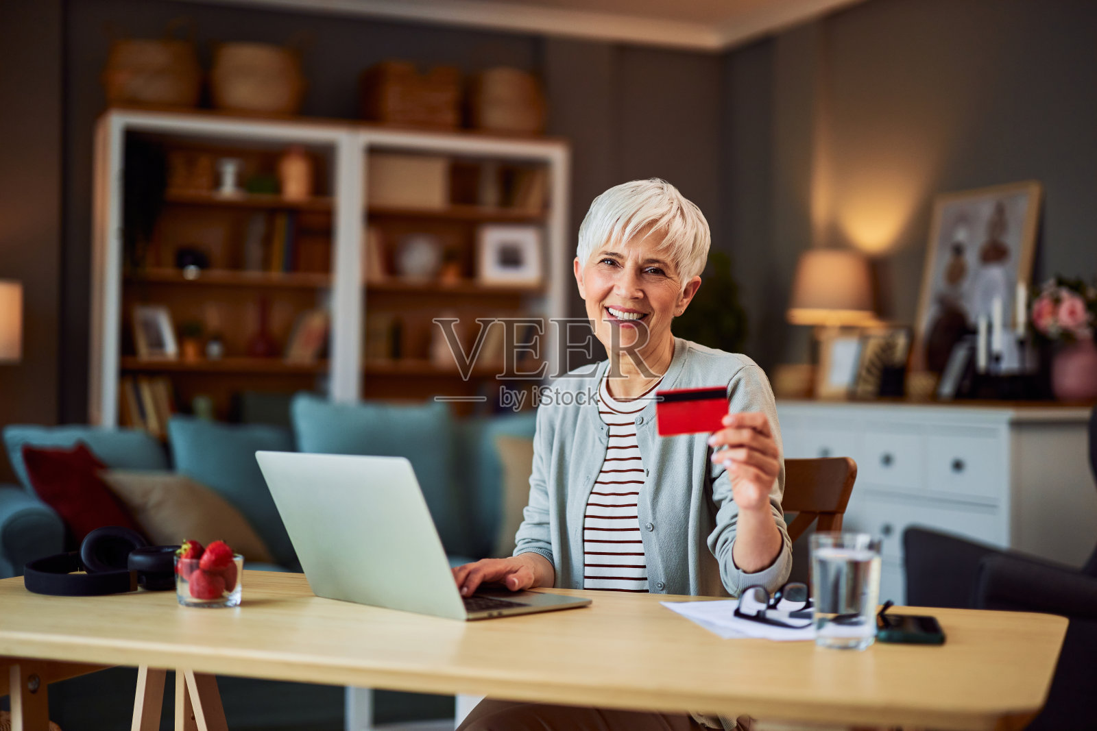 这幅画描绘的是一位兴高采烈的成年女性，她坐在办公桌前，用笔记本电脑和信用卡在网上购物照片摄影图片