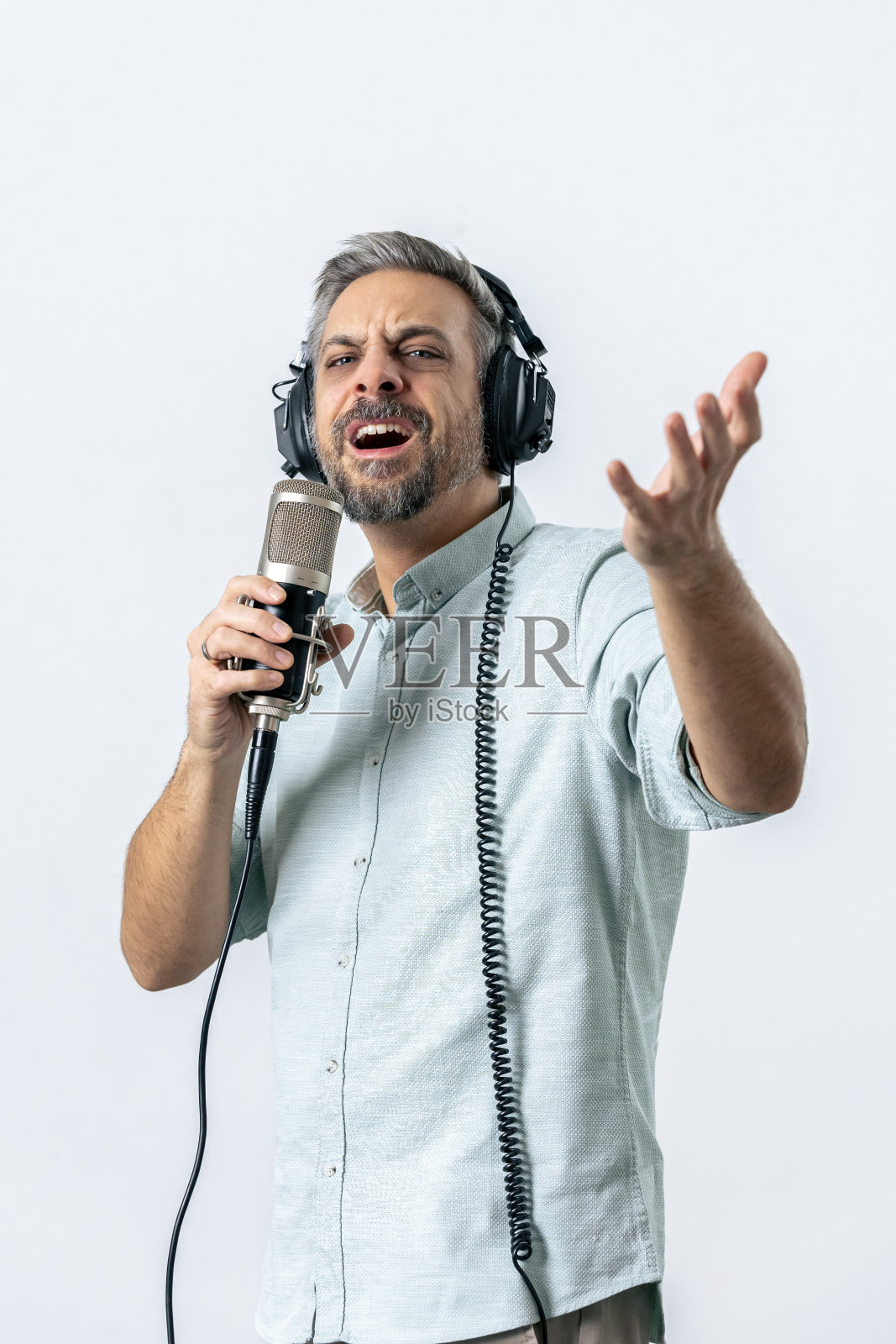 帅哥戴着耳机对着麦克风唱歌，背景是白色的。照片摄影图片