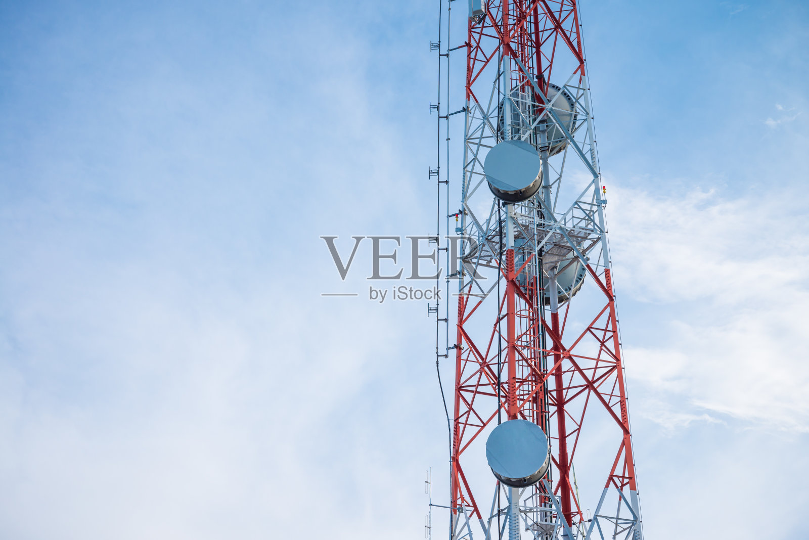 蓝蓝的天空背景下的红白电信塔。照片摄影图片