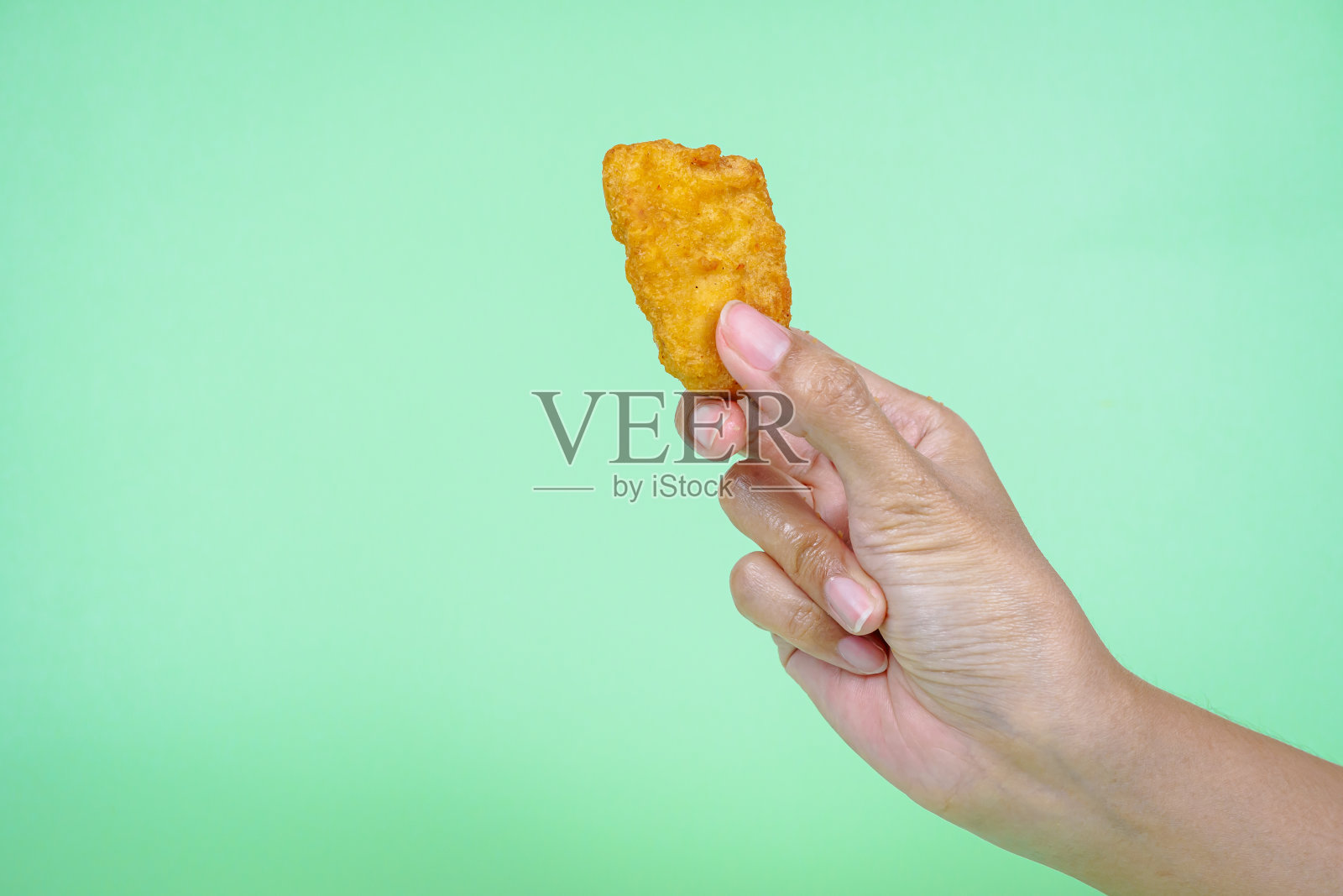 女性的手拿着绿色背景的炸鸡块。照片摄影图片