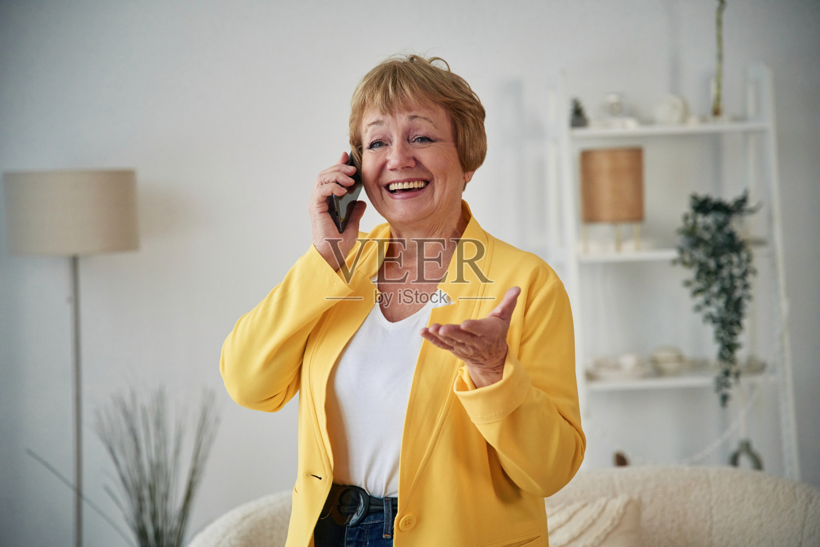 通过电话交谈。一位年长的妇女在家里的客厅里照片摄影图片