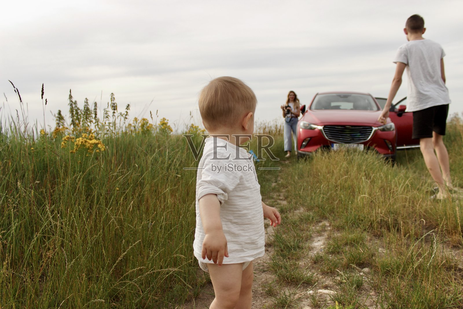 一家人开着一辆红色的小汽车到田野里消遣，一个小孩子回头看照片摄影图片