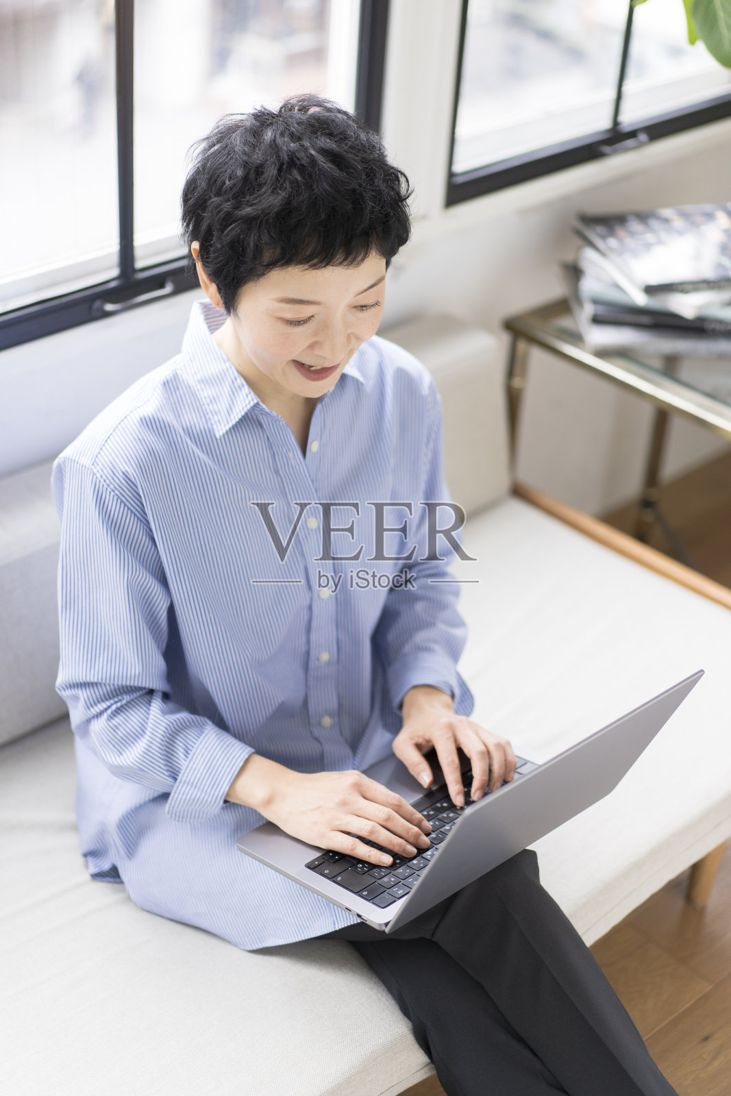 一位女士坐在家里客厅的沙发上用笔记本电脑工作。照片摄影图片